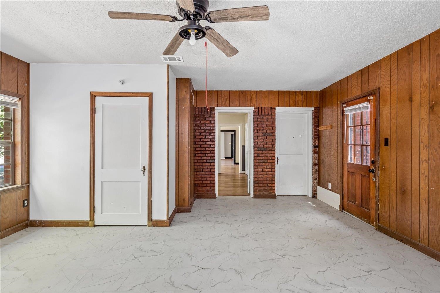 Empty room with wood-paneled walls, brick doorway, ceiling fan, and marble-look flooring.