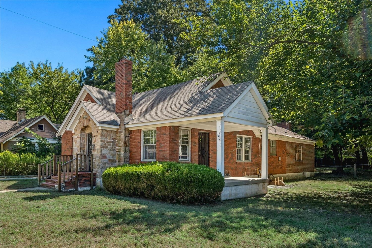 Red brick and stone house with a covered front porch, gabled roof, and mature trees.