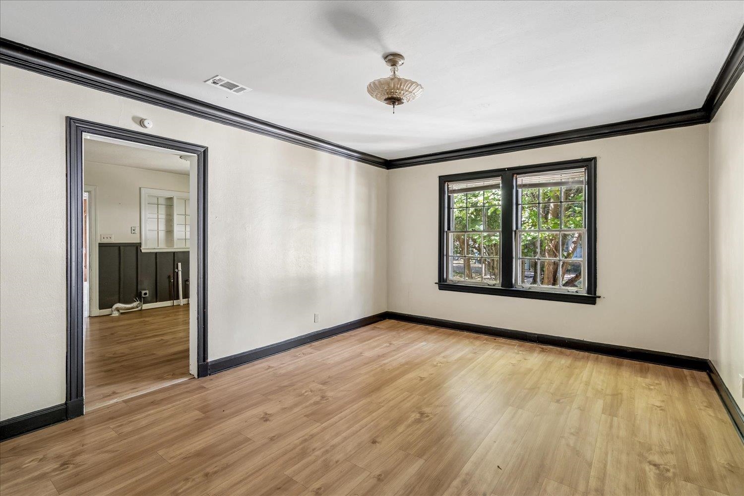 Empty room with wood flooring, dark trim, and two windows overlooking greenery.