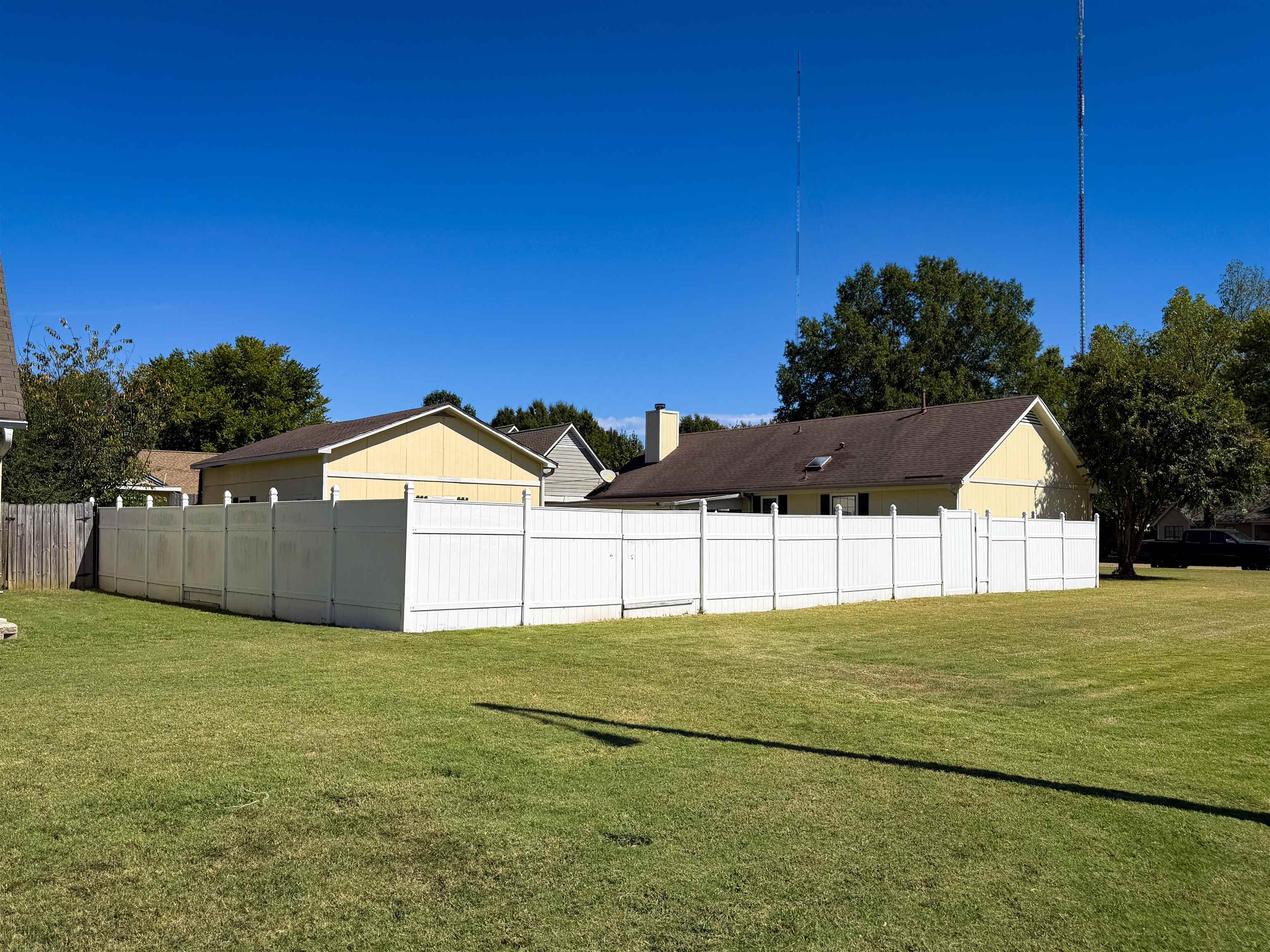 Backyard with a broad lawn, white privacy fence, and yellow house.