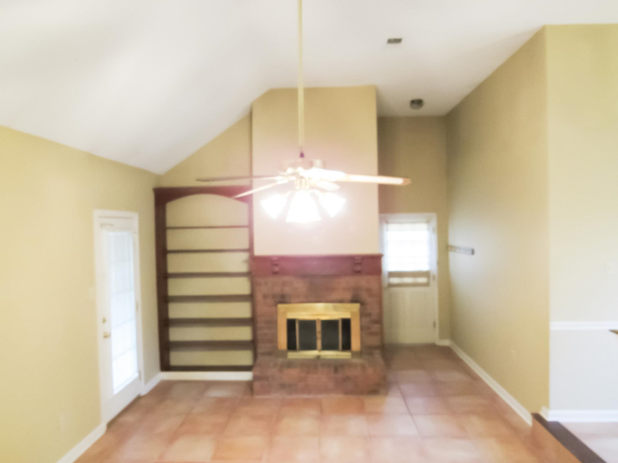 Vacant living room with a brick fireplace, built-in shelves, and a vaulted ceiling.