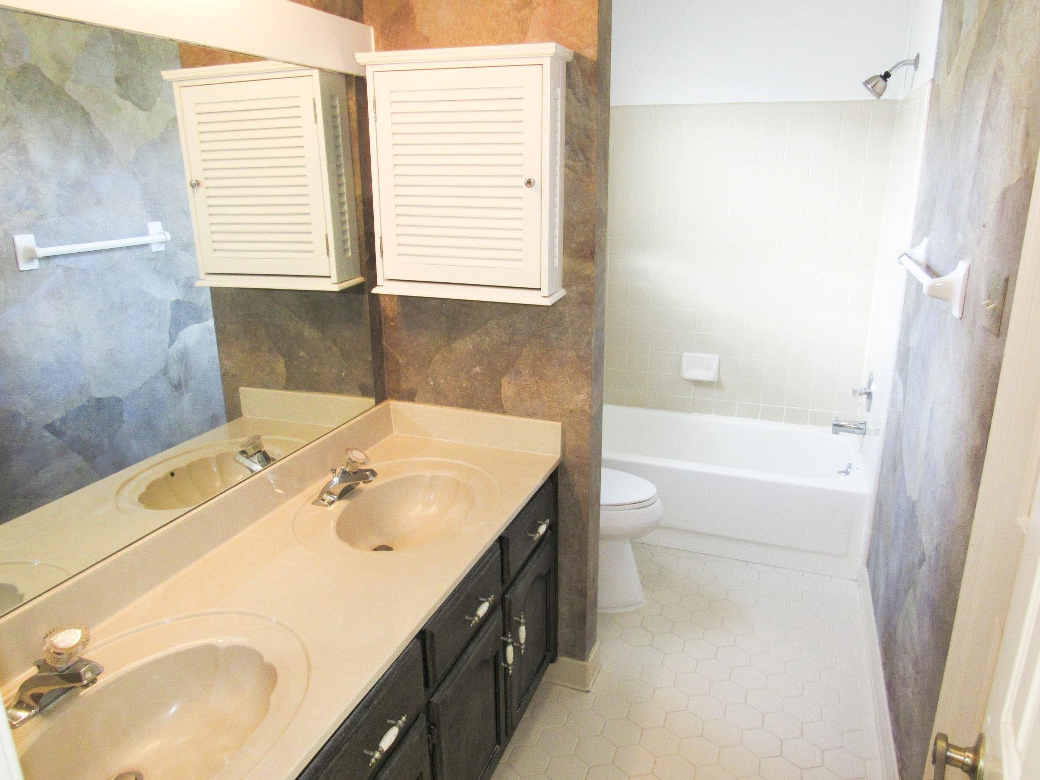 Bathroom with a double-sink vanity, large mirror, and bathtub with tiled surround.