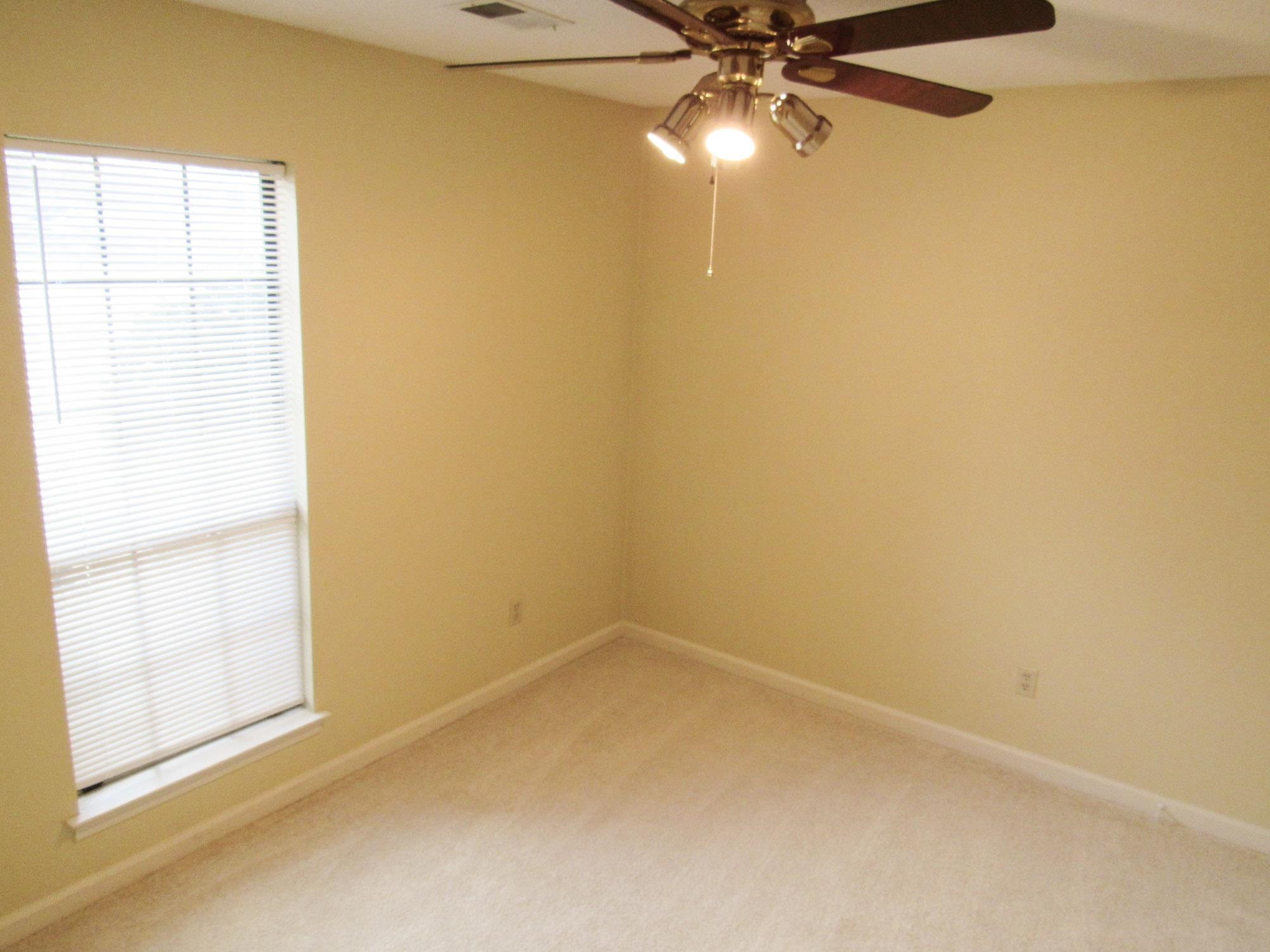 Empty carpeted room with pale yellow walls, window blinds, and a ceiling fan with light.