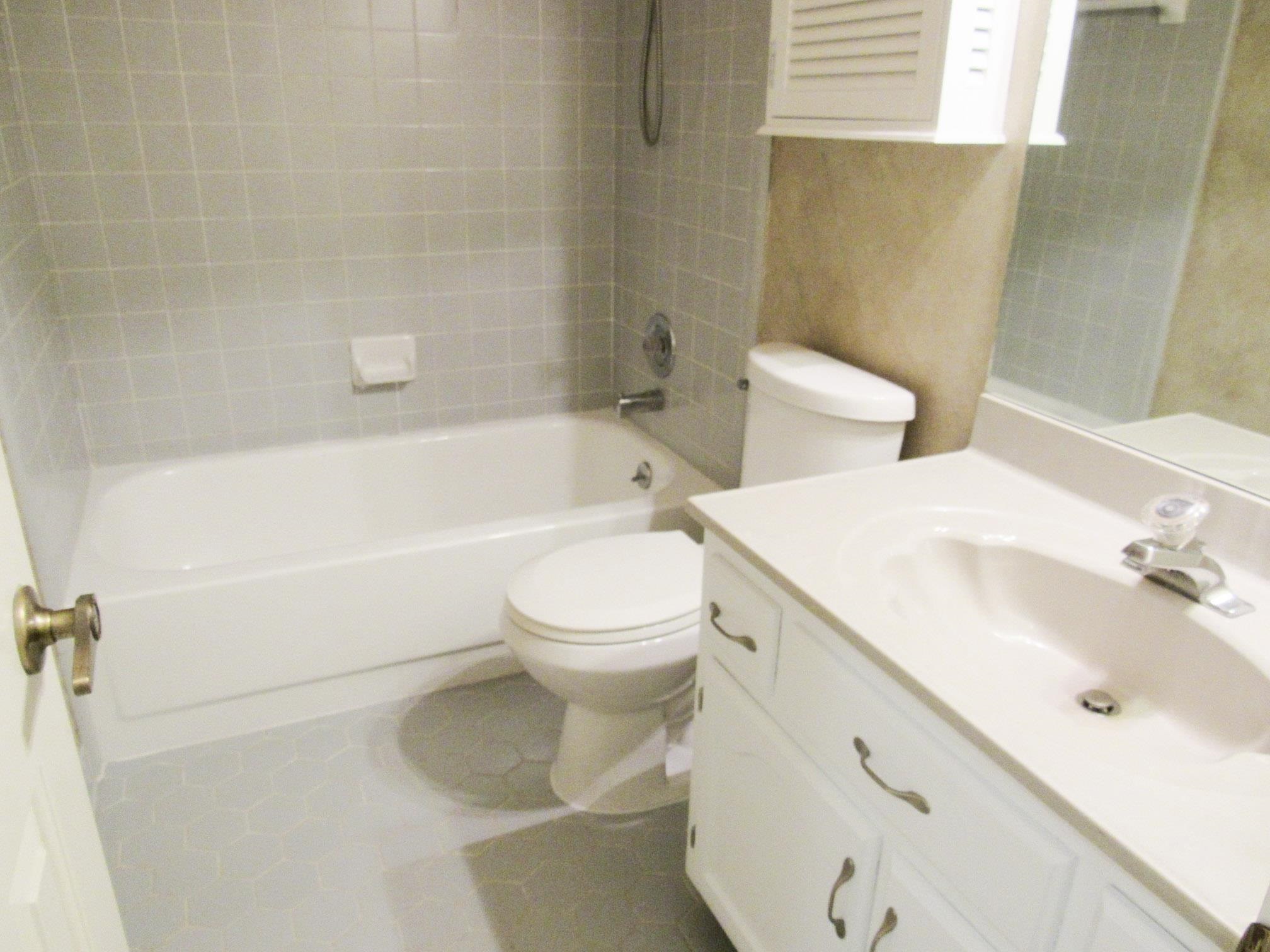 Bathroom with a tiled bathtub, toilet, and white vanity with an integrated sink.