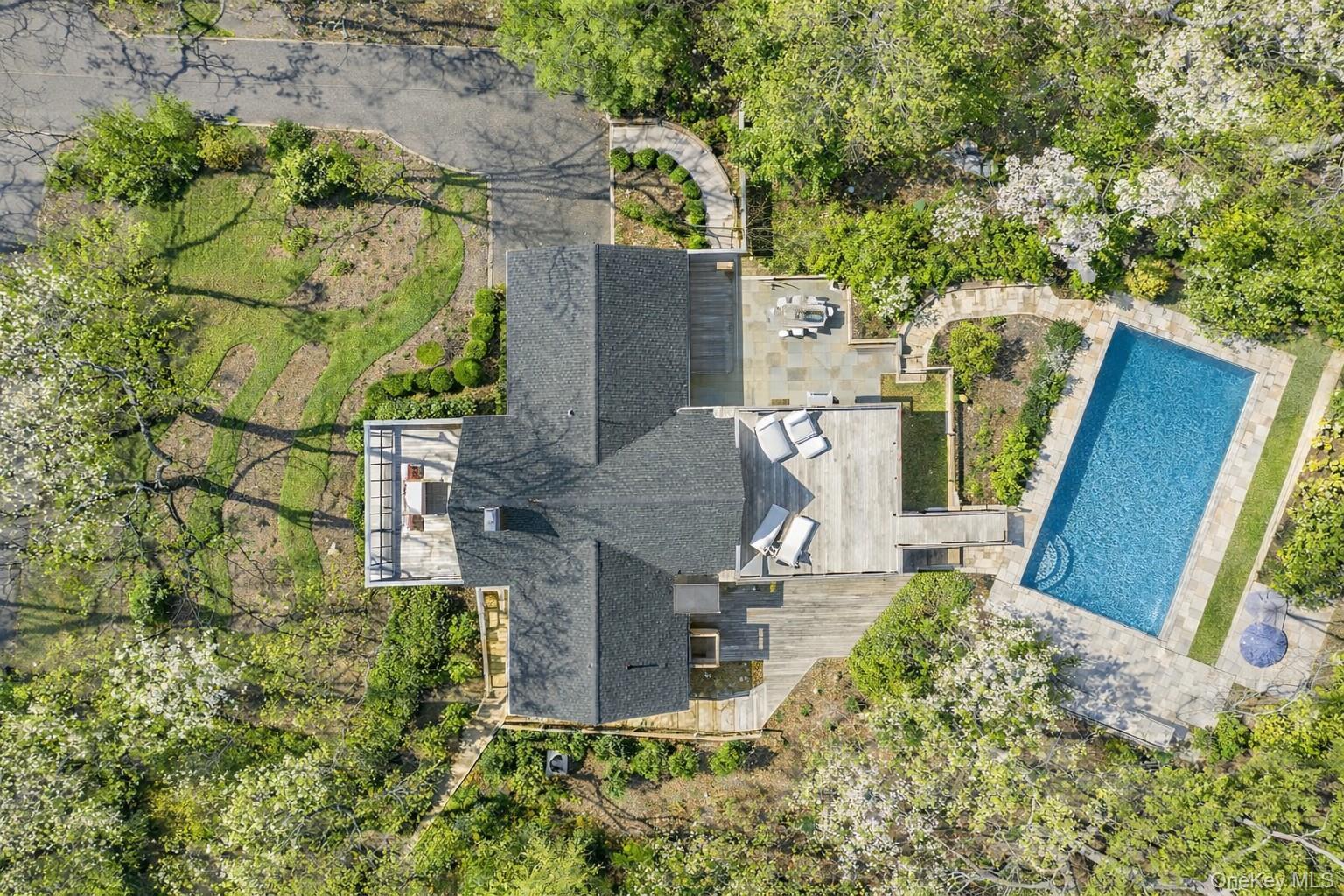 Aerial view of a landscaped East Hampton home with a stone patio and rectangular pool.