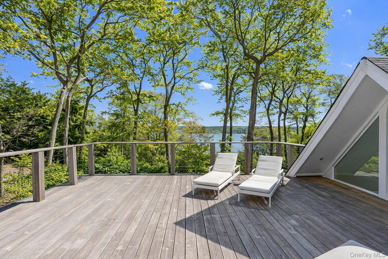 Wooden deck with white loungers overlooking water through leafy trees