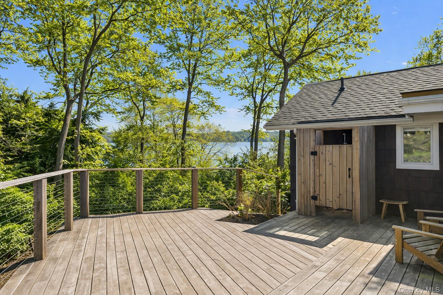 Wooden deck overlooking the water, with leafy trees and outdoor chairs.
