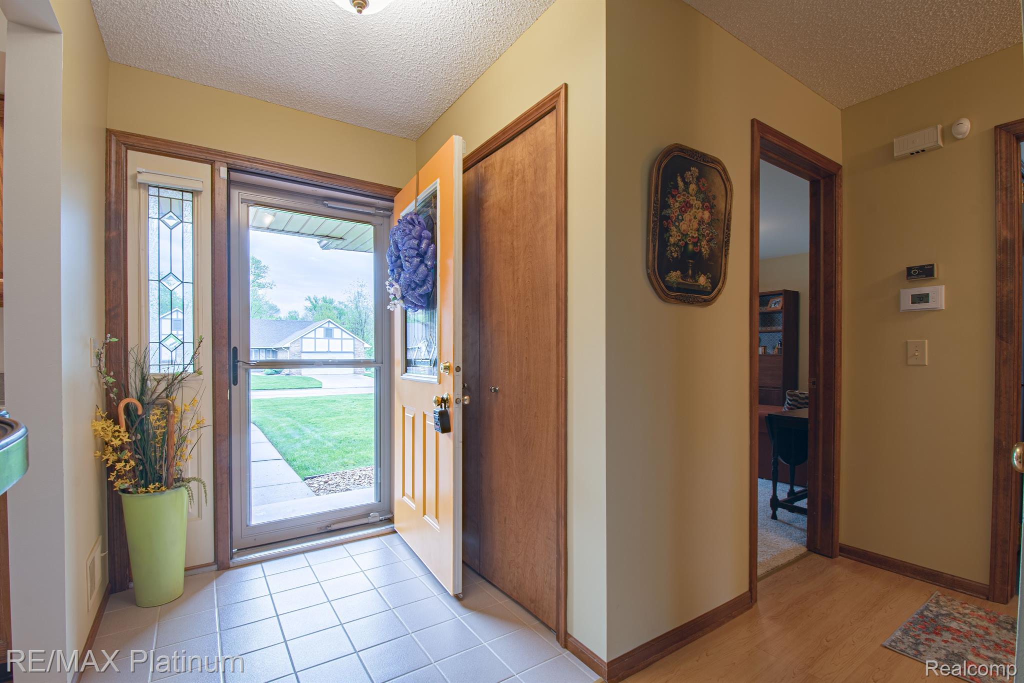 Entry foyer with tiled floor, open front door, decorative glass sidelight, and a view of the lawn.