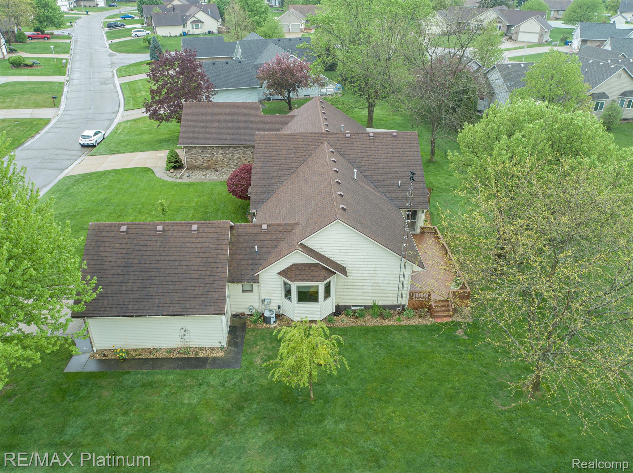 Aerial view of a light-colored house with a brown roof, rear deck, and expansive lawn.