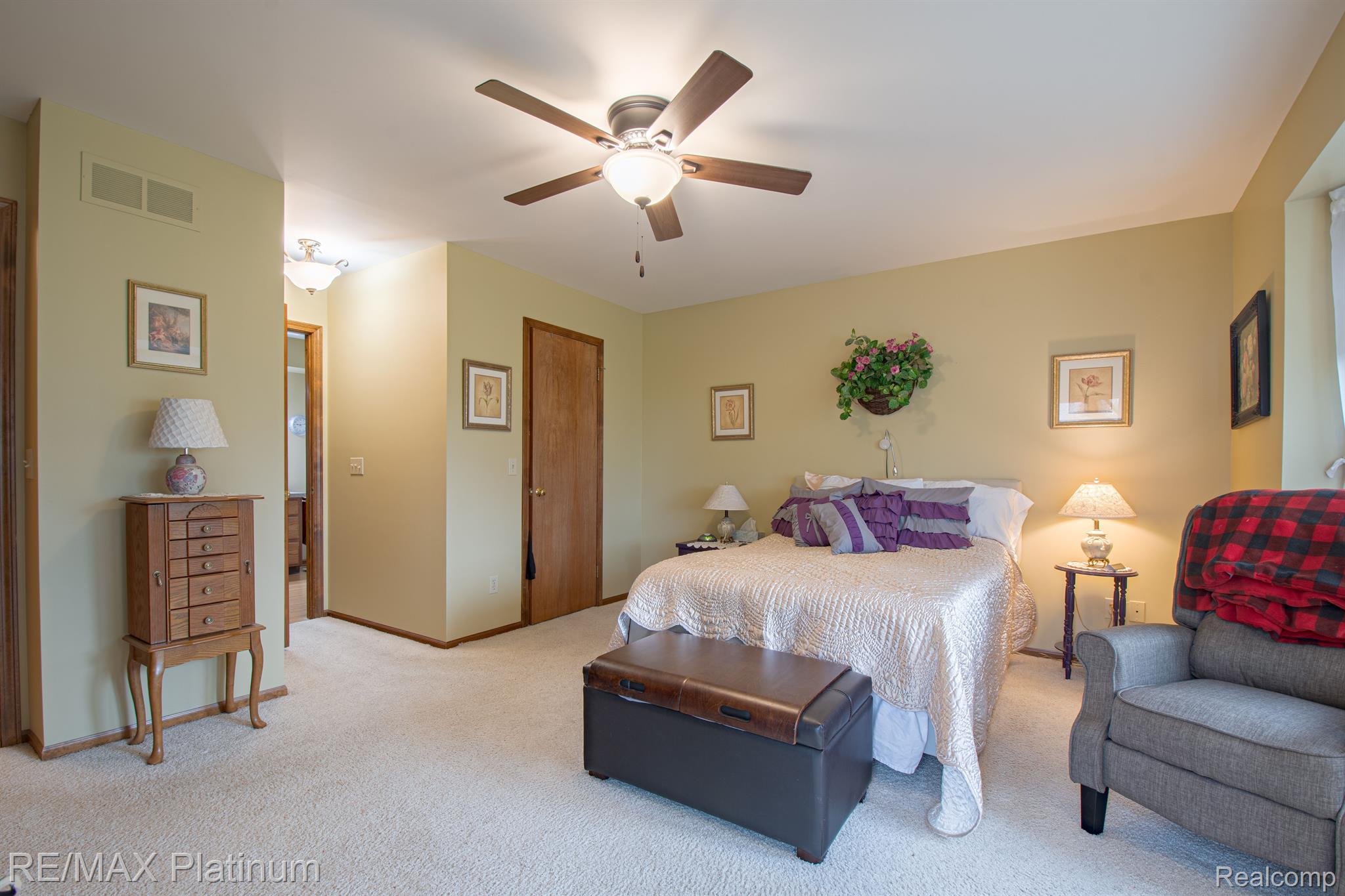 Furnished bedroom with a large bed, purple pillows, ceiling fan, and gray armchair.