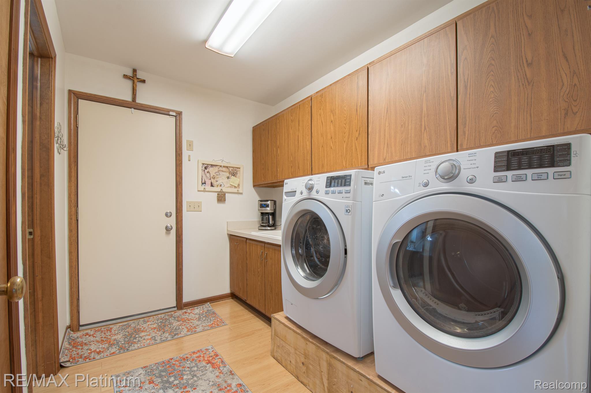 Laundry room with front-loading washer and dryer raised beside oak cabinets and an entry door.