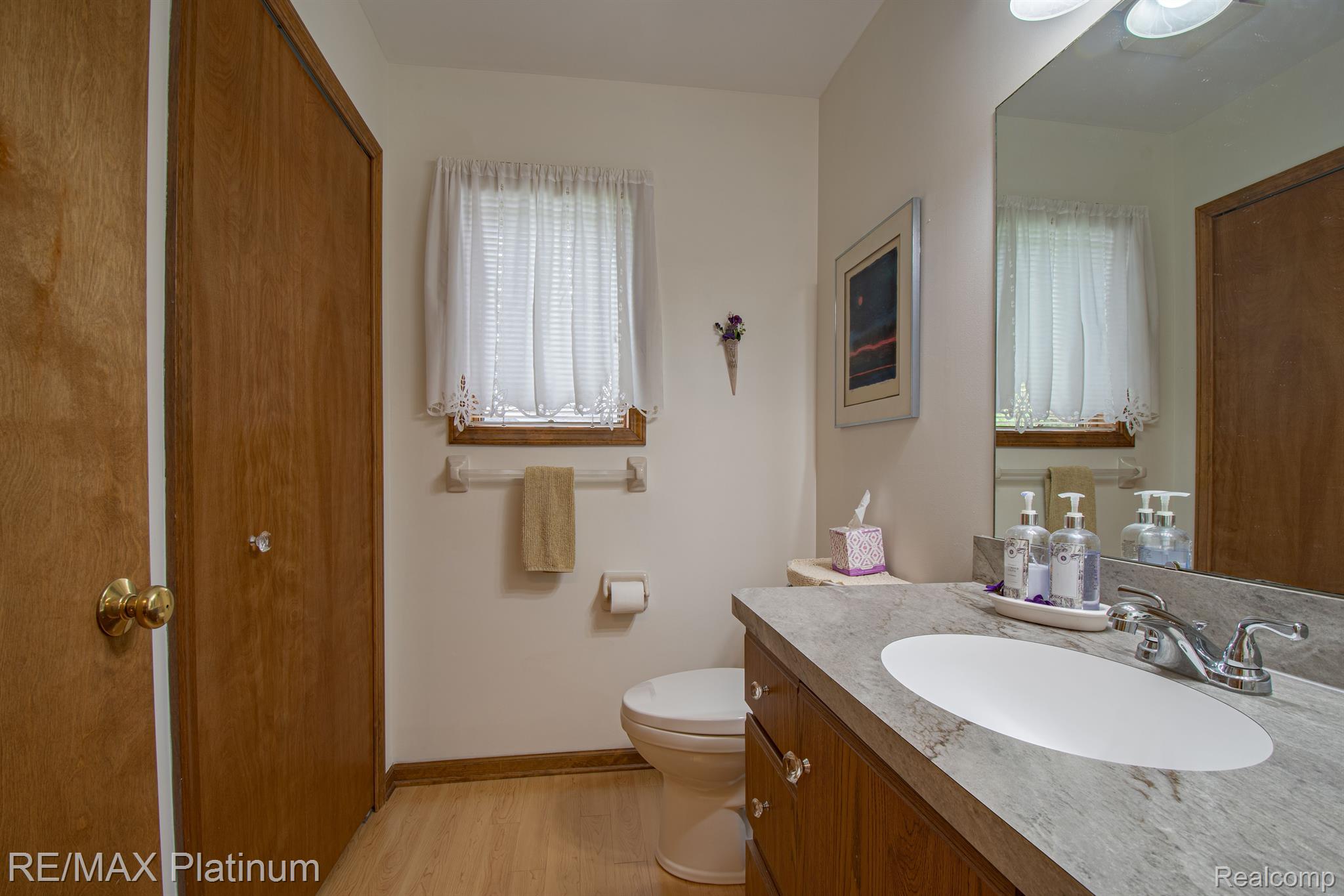 Bathroom with a wood vanity, oval sink, large mirror, and curtained window.