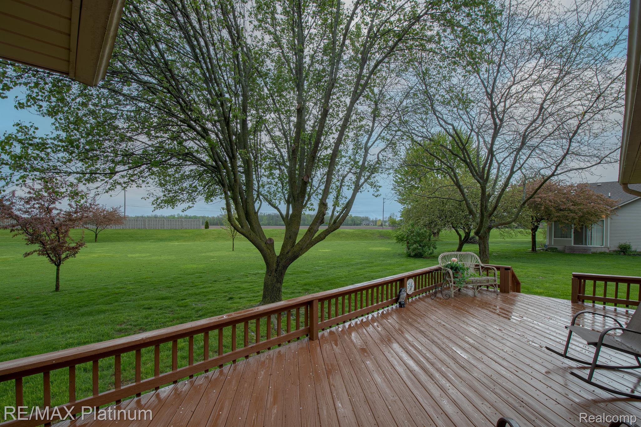 Wooden backyard deck with patio chairs overlooking a spacious lawn and mature trees.
