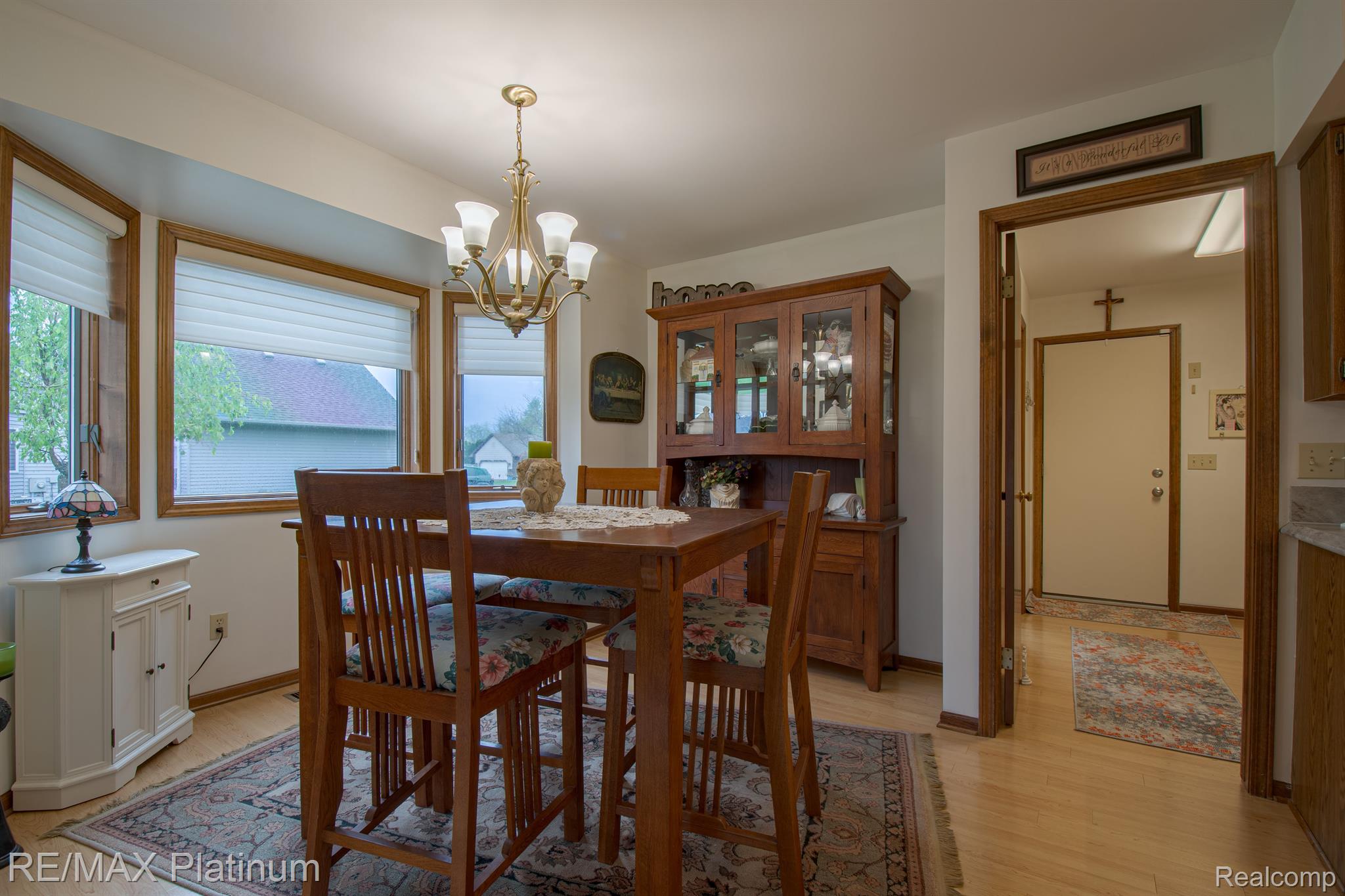 Dining room with a wooden table, glass-front china cabinet, chandelier, and large windows.