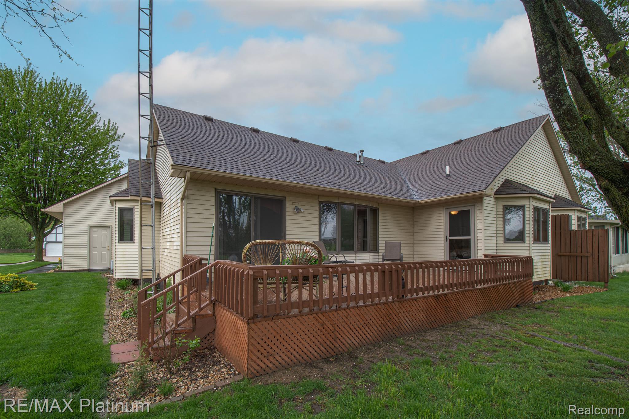 Rear exterior of a beige home with a raised wooden deck and lattice skirting.
