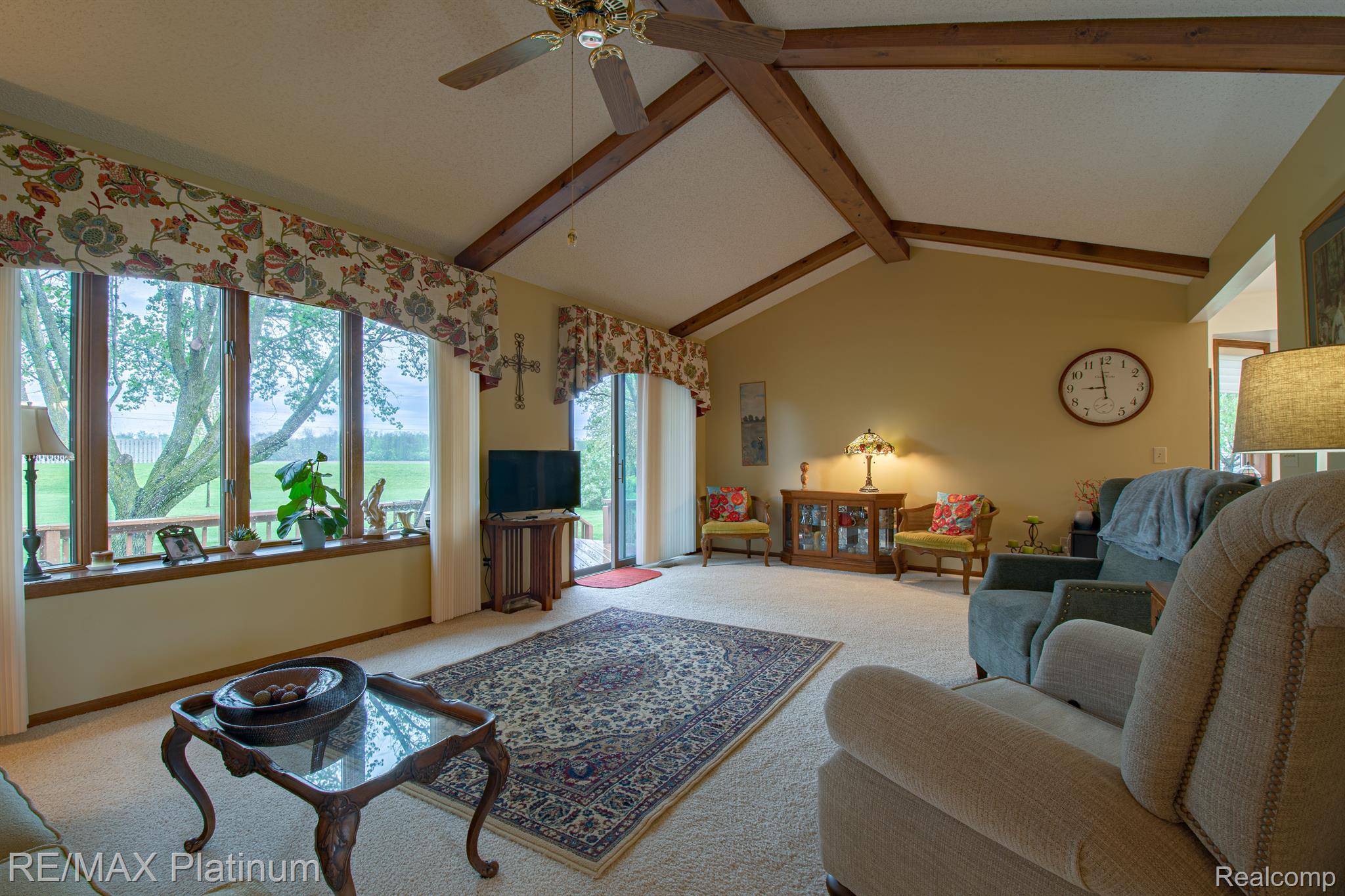 Living room with vaulted wood-beam ceiling, large windows, and a patterned rug.