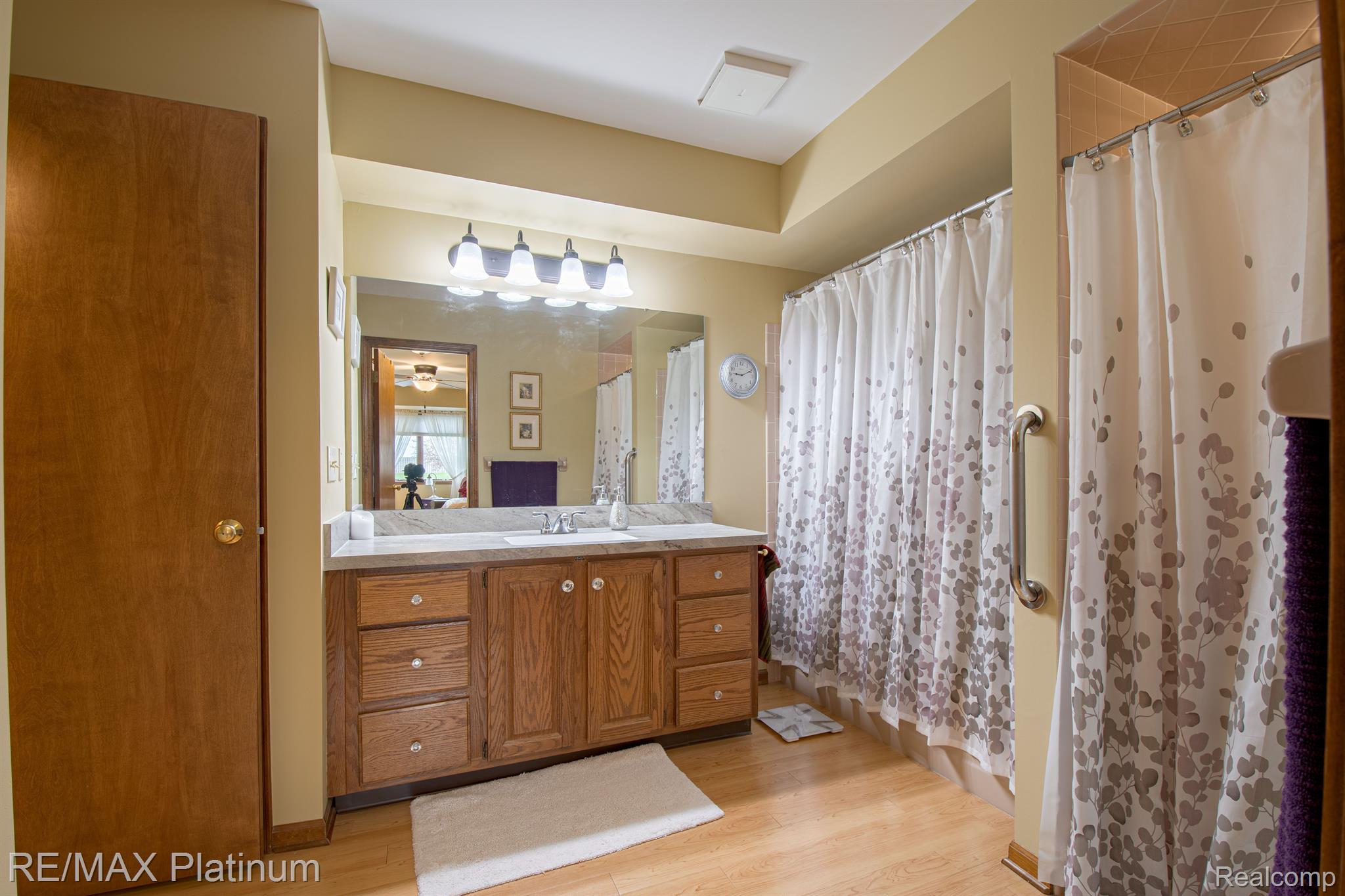 Bathroom with a large wood vanity and mirror beside a patterned shower curtain and grab bar.