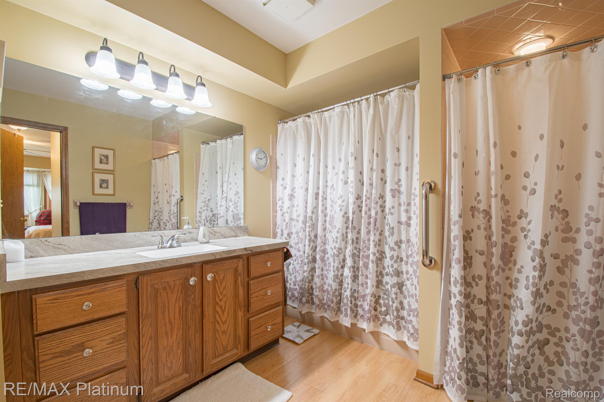 Bathroom with an oak vanity, large mirror, patterned shower curtains, and a grab bar.