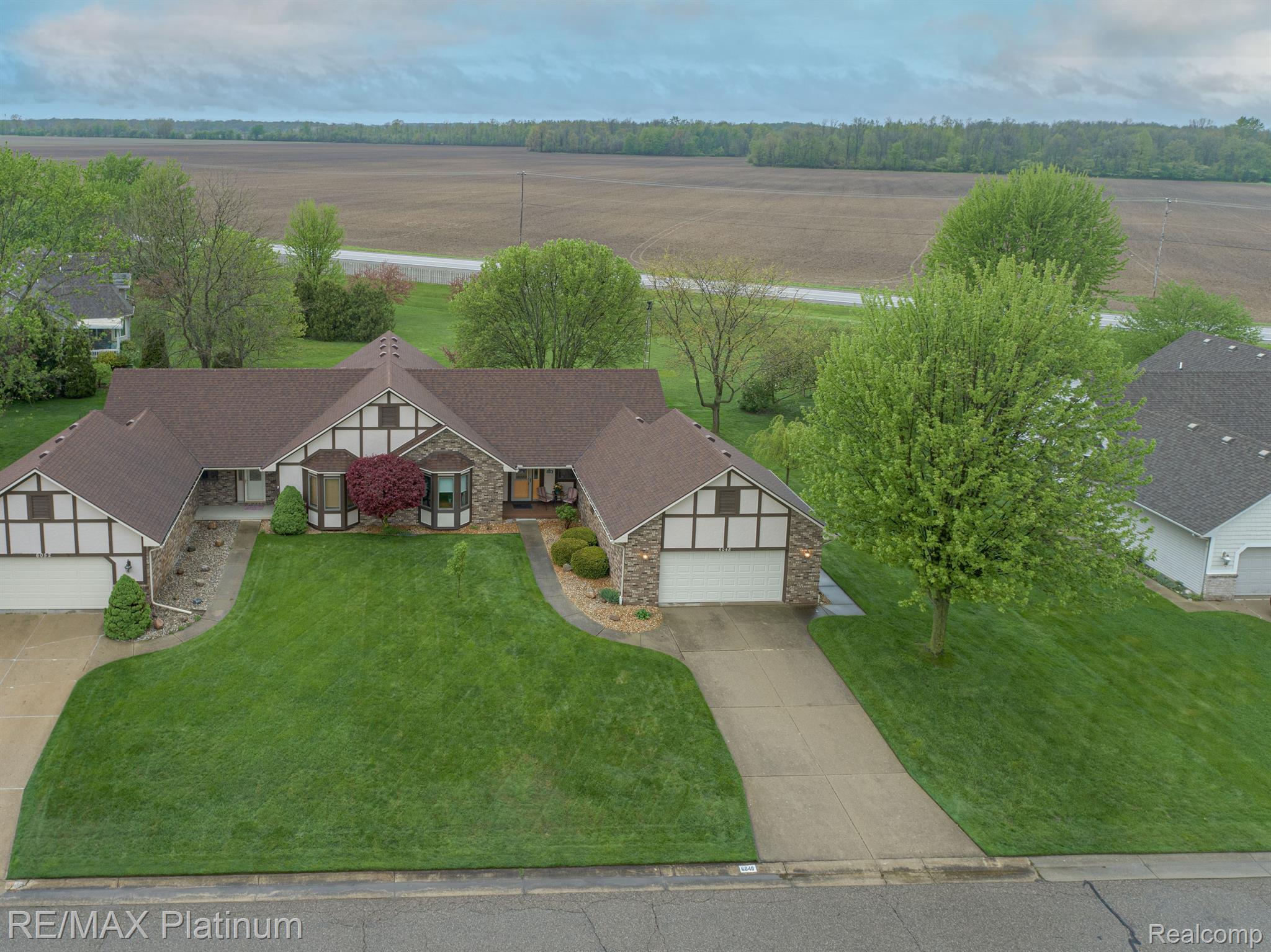 Aerial view of a sprawling brick-and-stucco home with two garages, a broad lawn, and a long driveway.