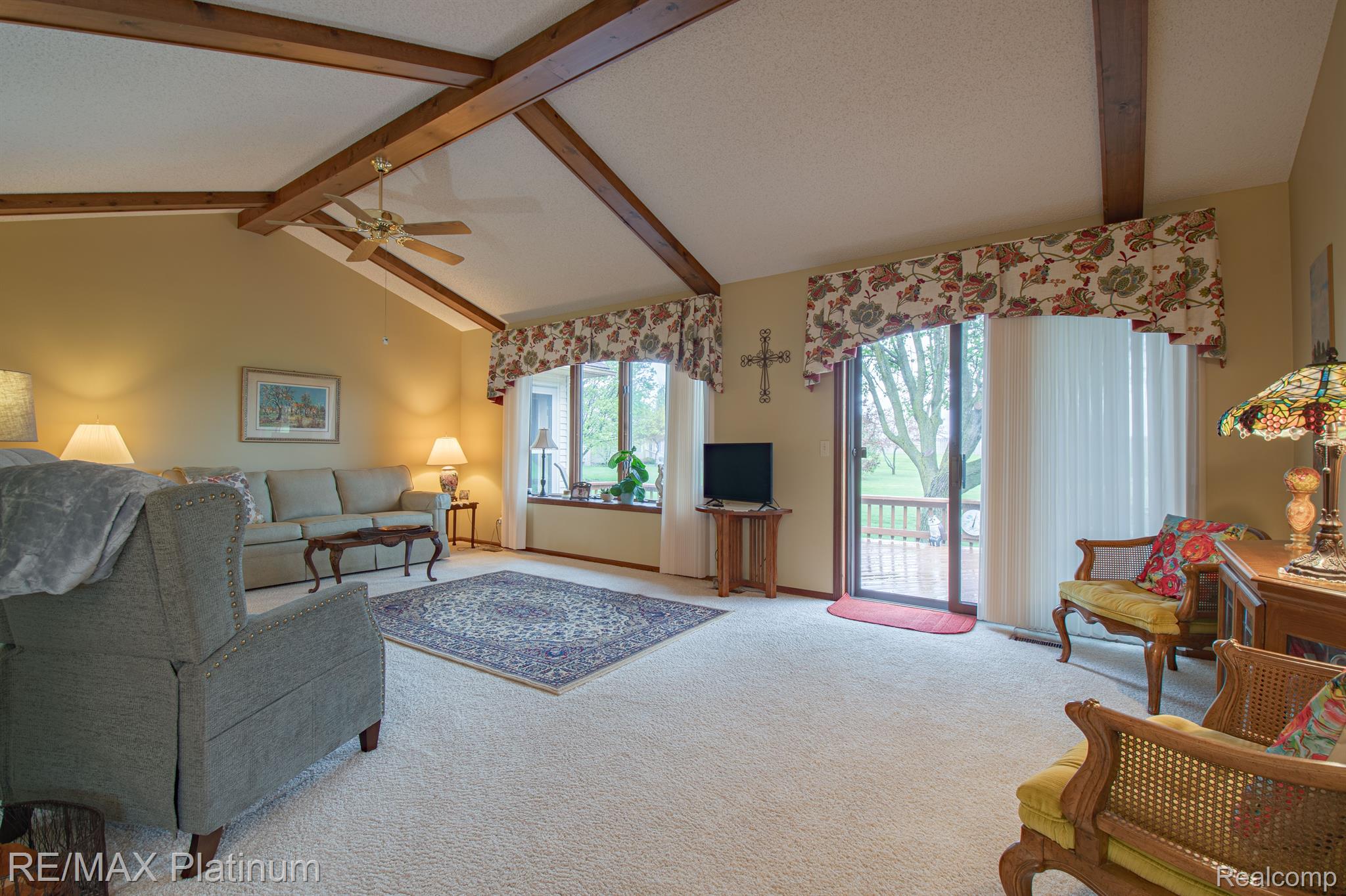 Living room with vaulted wood-beam ceiling, furnished seating, and sliding doors to a deck.
