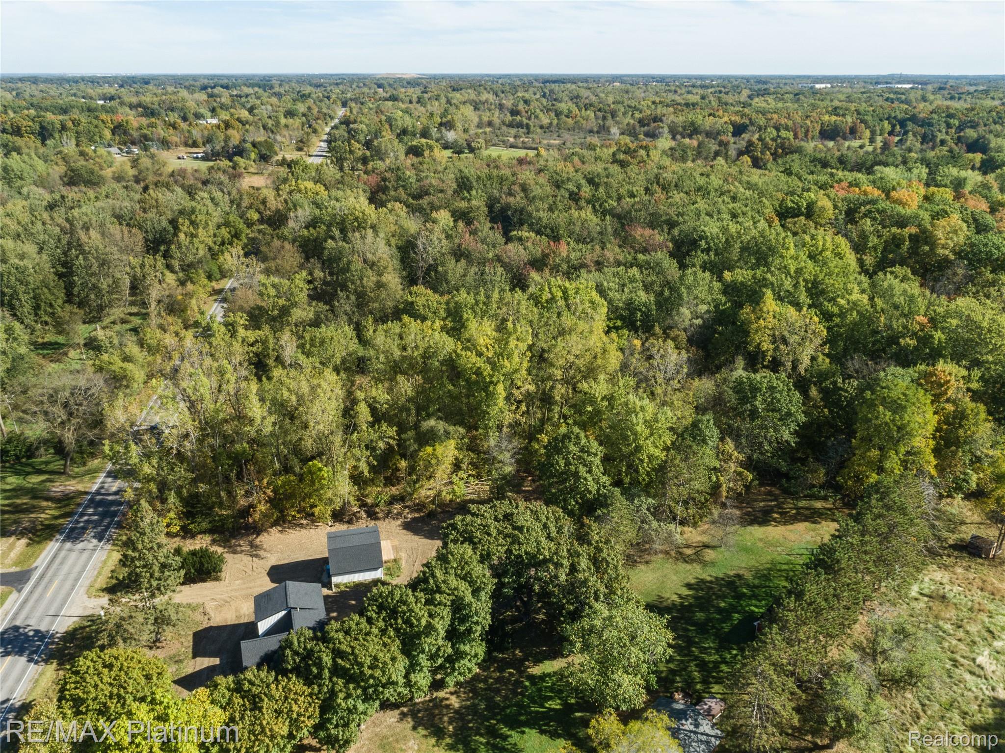 Aerial view of wooded property with a roadside, cleared areas, and several small buildings.