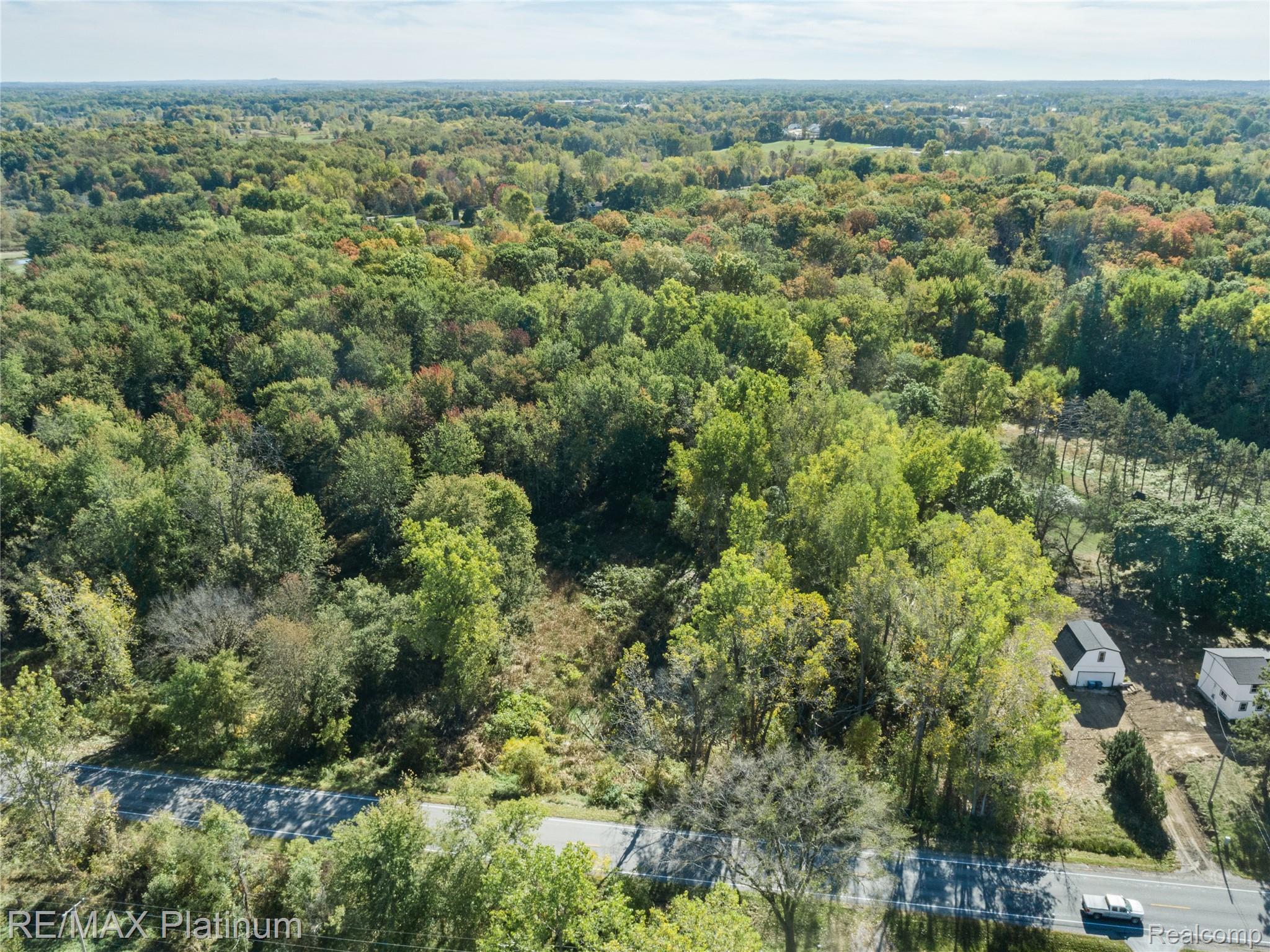 Aerial view of wooded land along a paved road, with two small white outbuildings.