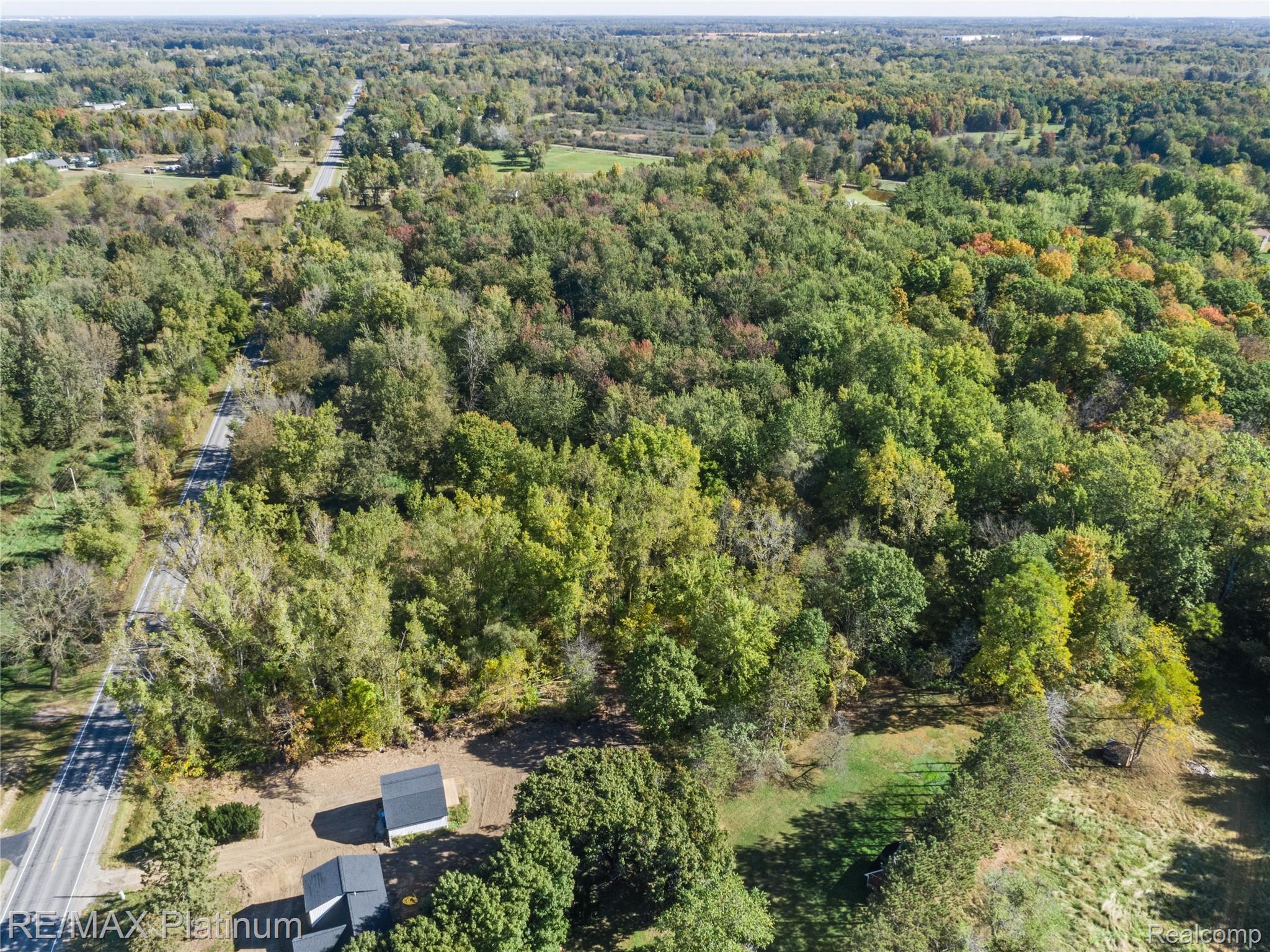 Aerial view of wooded land with a roadside and two small buildings.