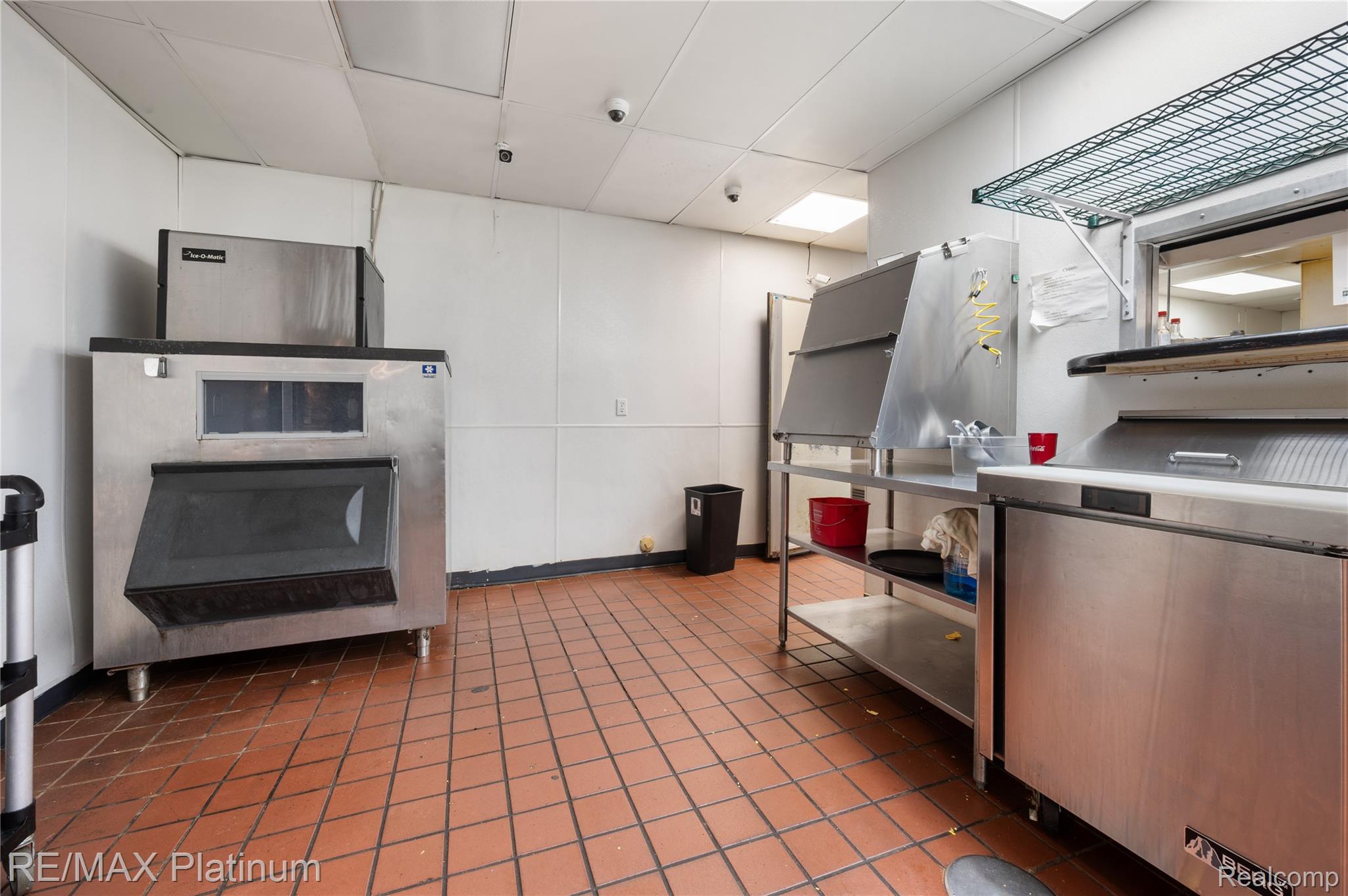 Commercial kitchen with stainless-steel equipment, a large ice machine, and reddish-brown tile flooring.