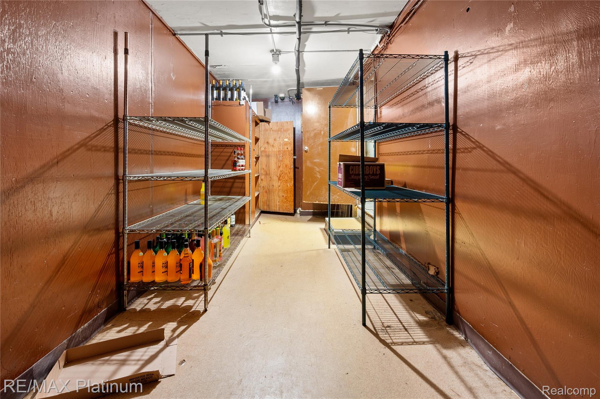 Storage room with metal wire shelving, beverage bottles, and brown-painted walls.
