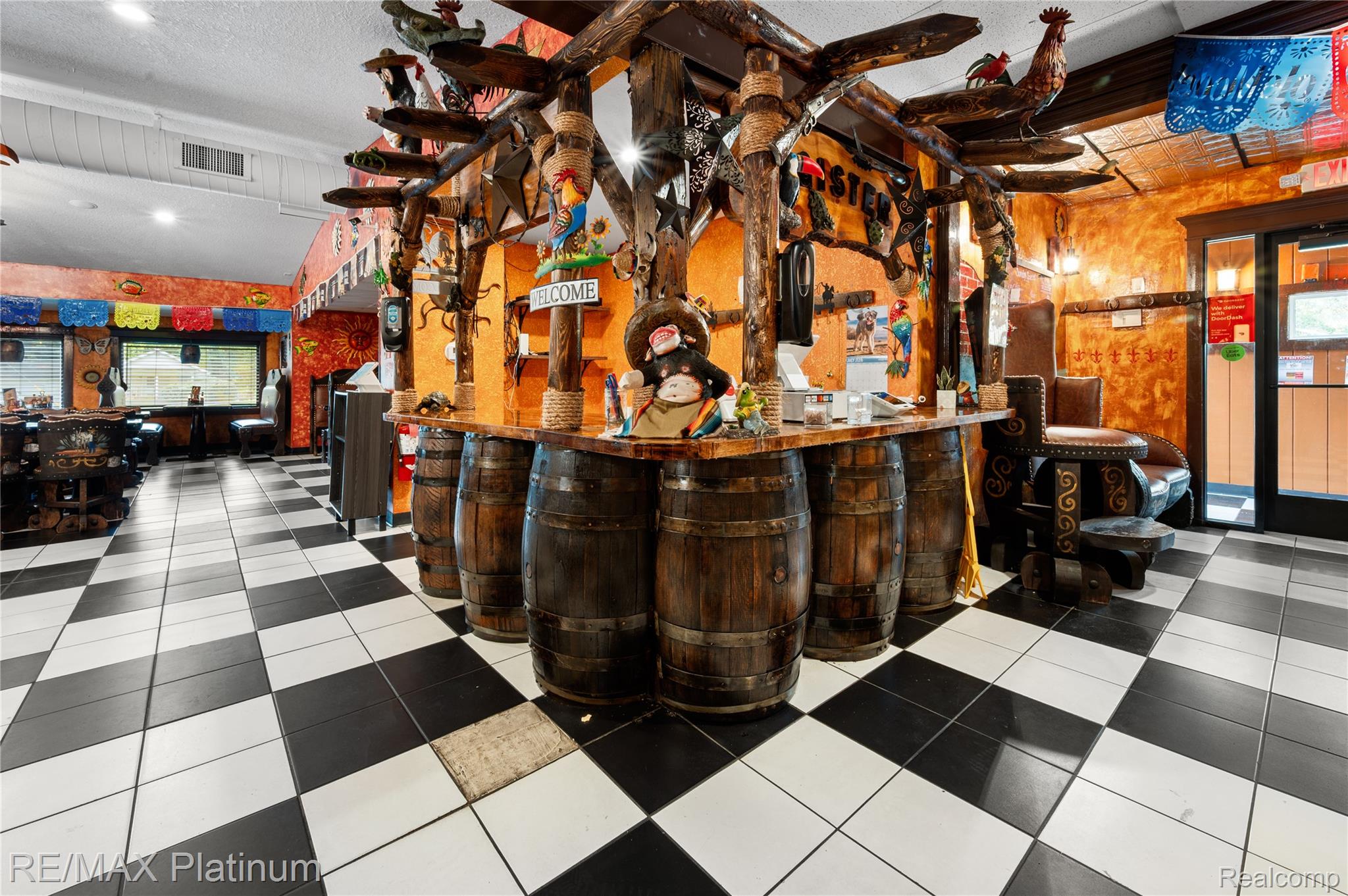 Restaurant interior with a barrel-front counter, rustic decorations, and black-and-white checkered flooring.