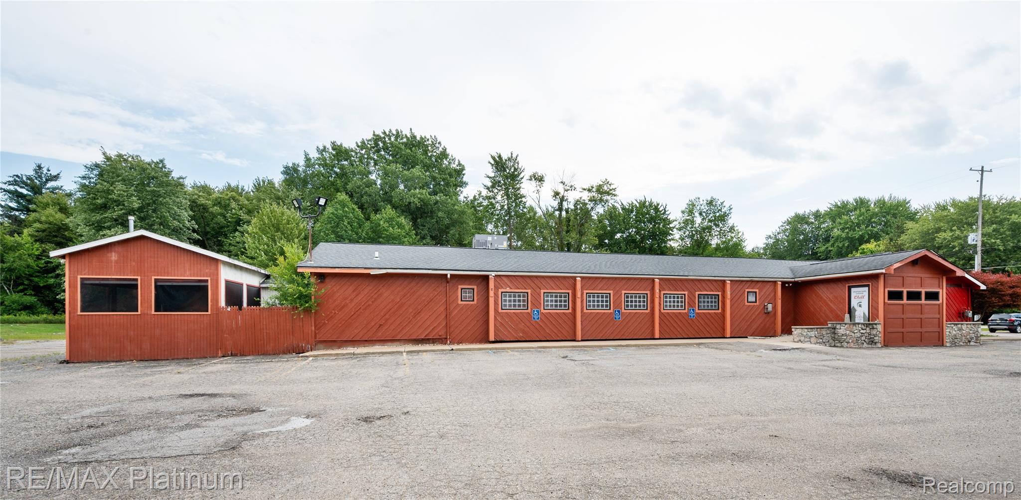 Long red commercial building with a gray roof, rows of windows, and a paved parking area.