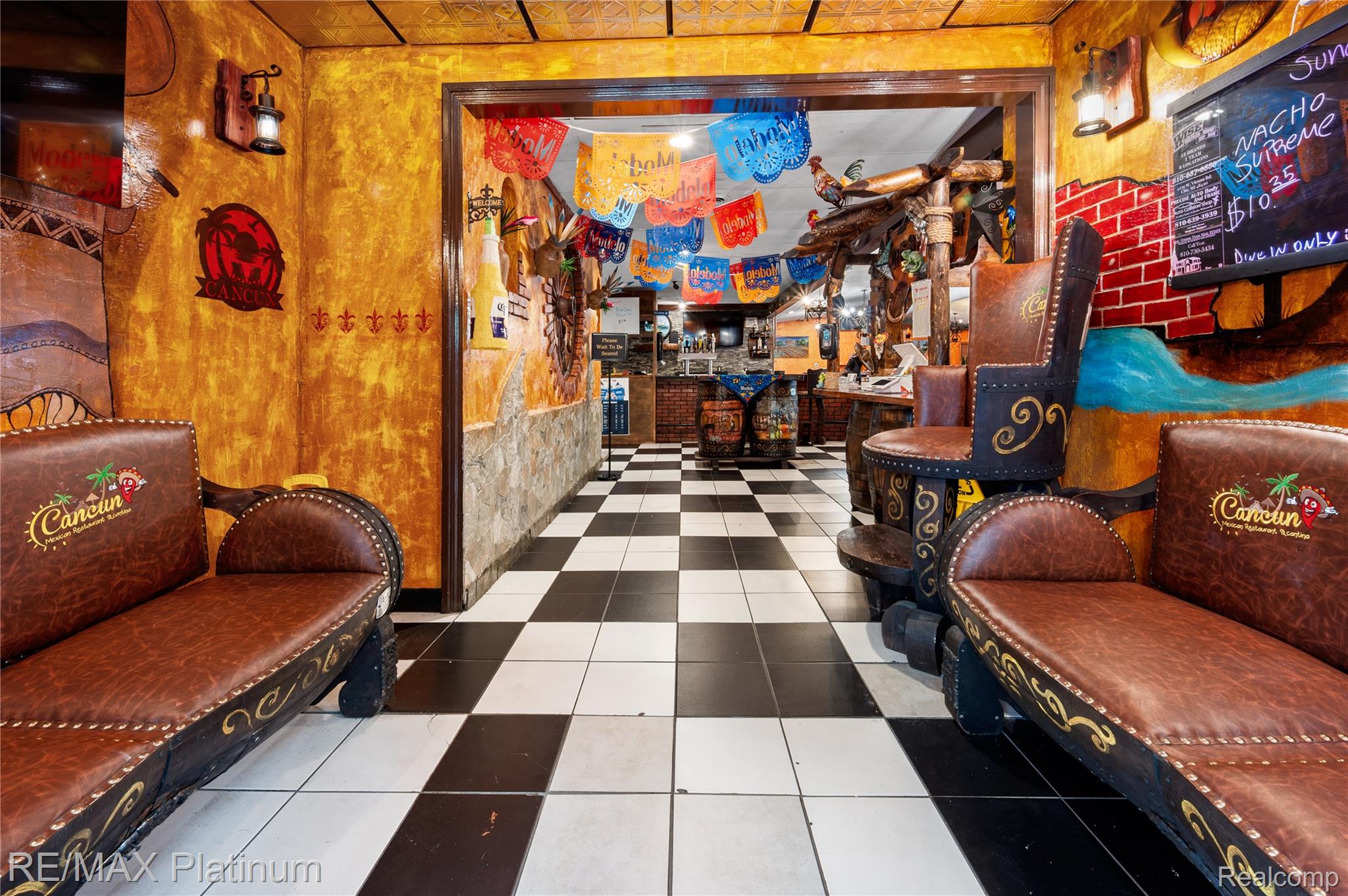 Restaurant interior with leather seating, checkered tile, orange walls, and colorful hanging banners.