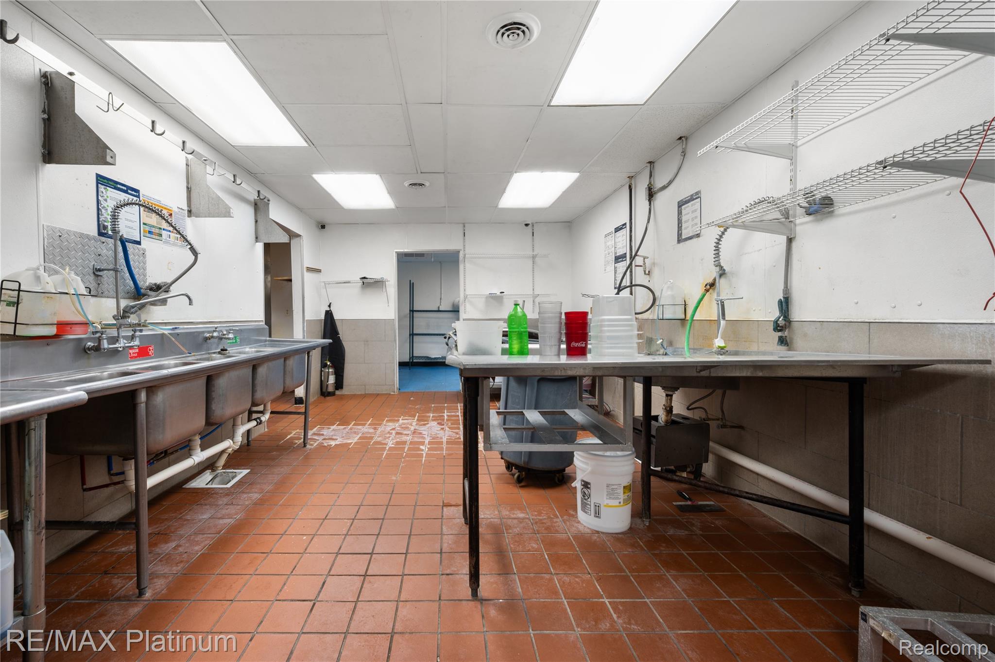Commercial kitchen with stainless-steel sinks, a worktable, and wire shelving.
