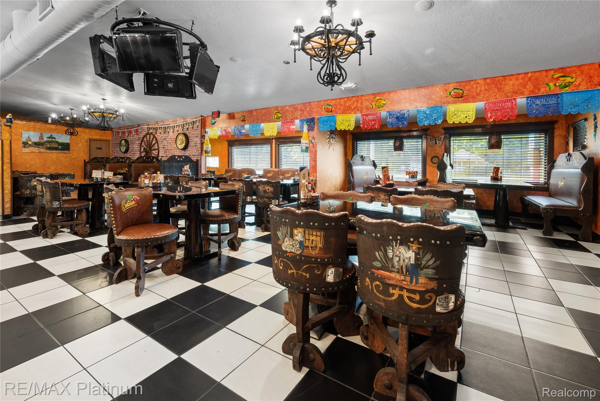 Restaurant dining room with ornate leather chairs, black-and-white tile, and colorful hanging decorations.