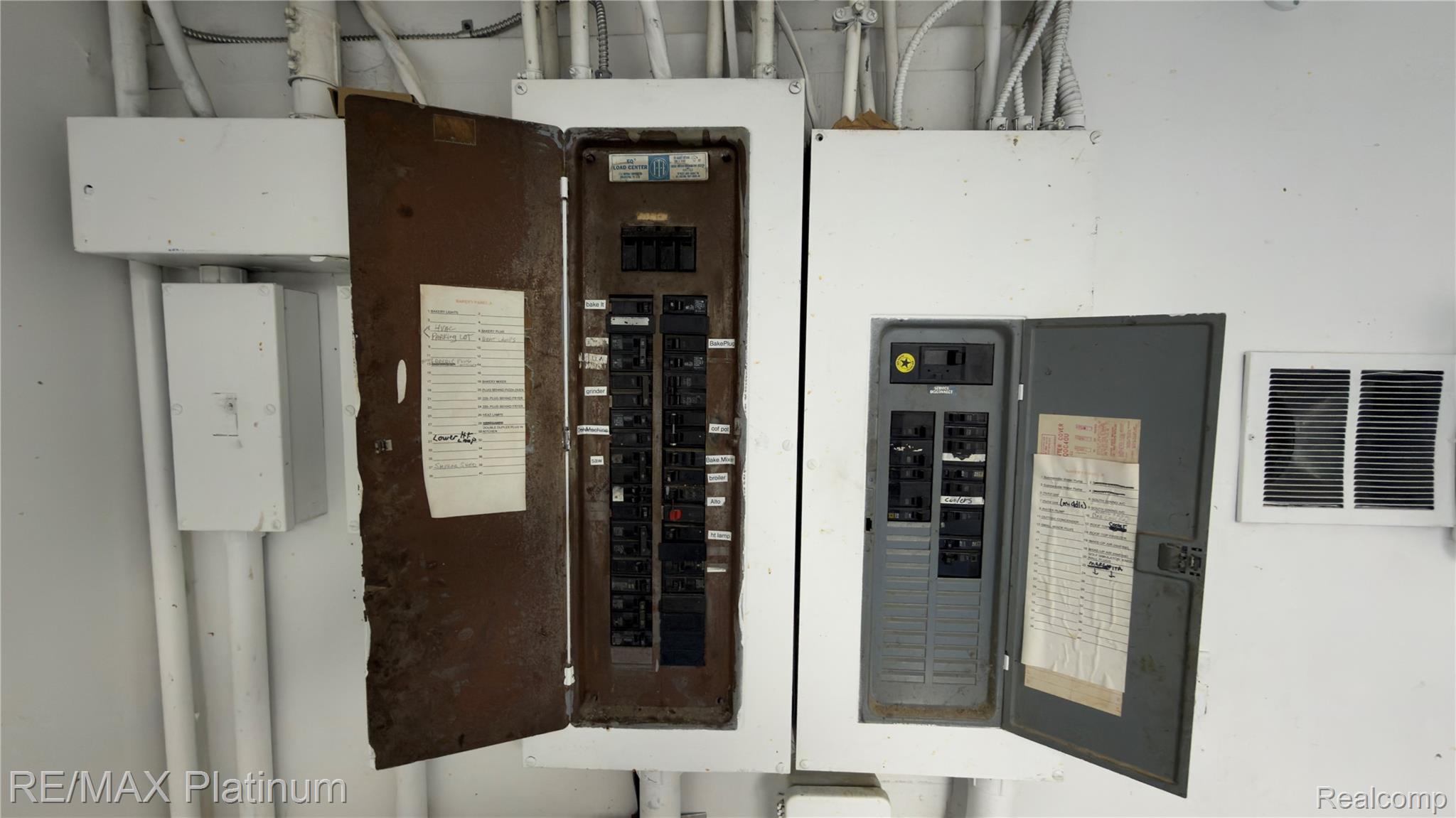 Two open electrical breaker panels with labeled circuits and wiring conduits above.