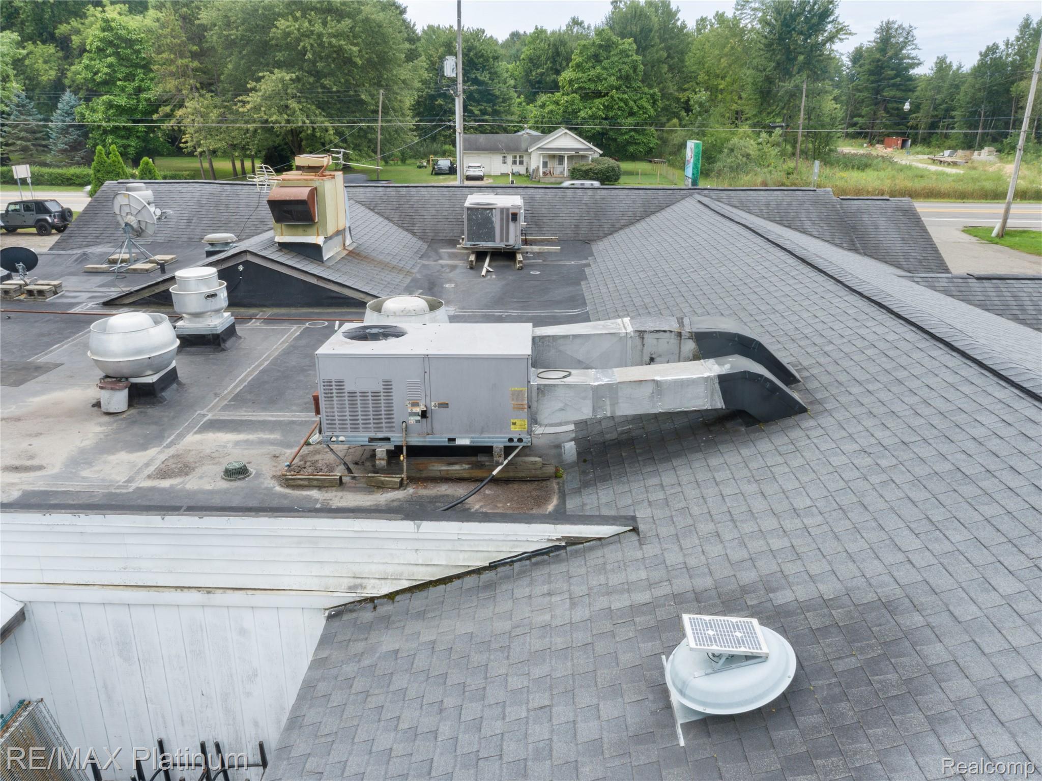 Building roof with gray shingles, flat sections, rooftop HVAC equipment, vents, and satellite dishes.
