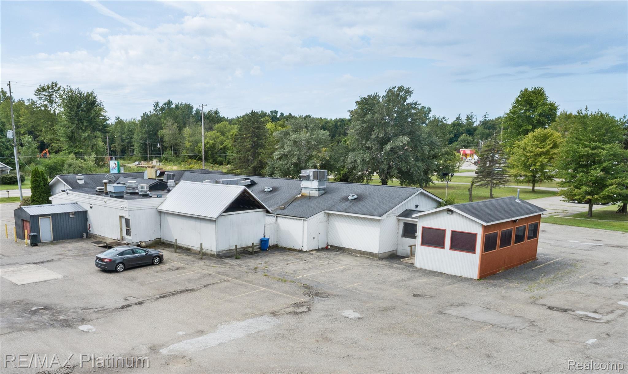 Aerial view of a low commercial building with a large paved parking area and trees.
