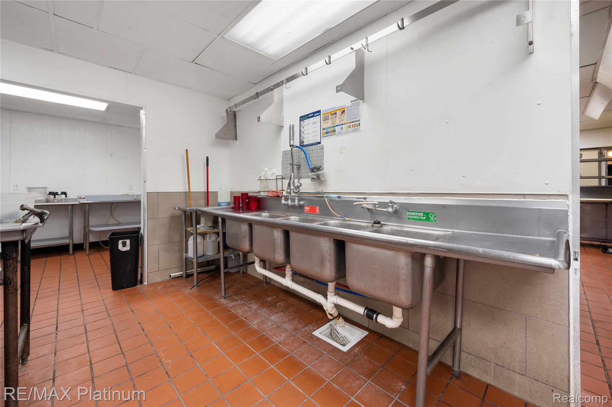Commercial kitchen with a long stainless-steel sink and terracotta-colored tile floor.