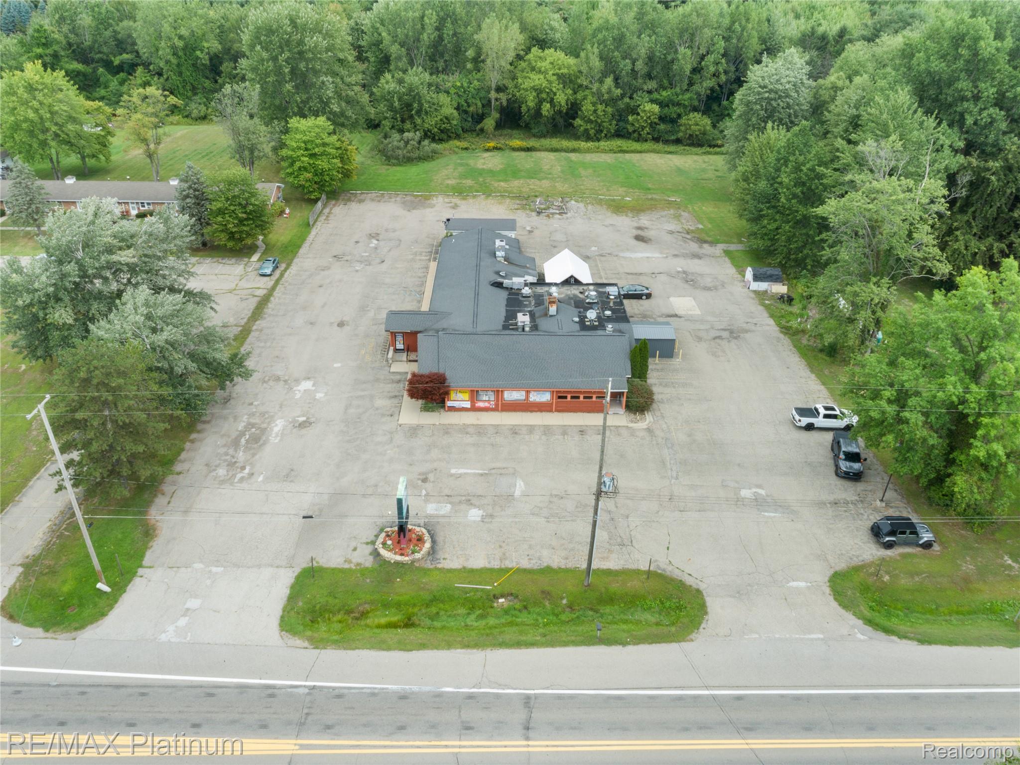 Aerial view of a commercial building with a broad parking lot and wooded surroundings.