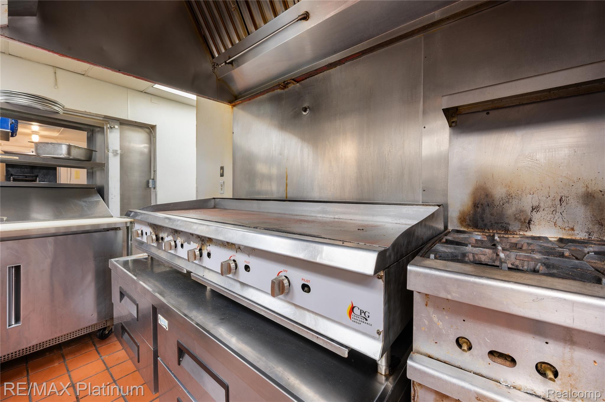 Commercial kitchen with a stainless-steel griddle, gas range, and large exhaust hood.