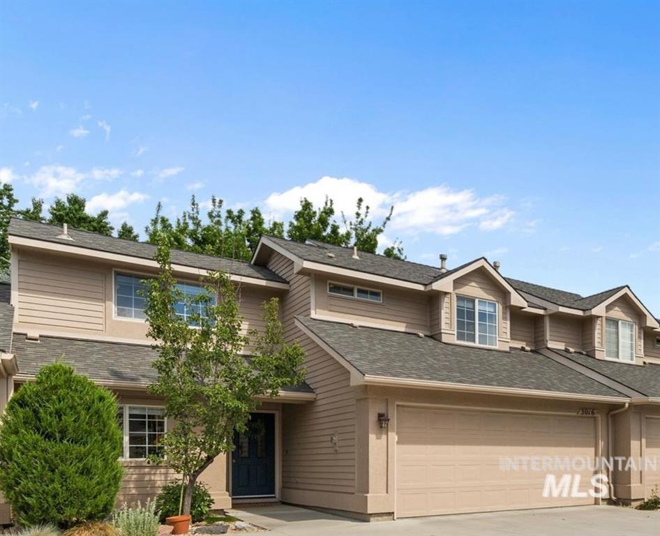 Beige two-story home with a two-car garage, dark front door, and landscaped front yard.