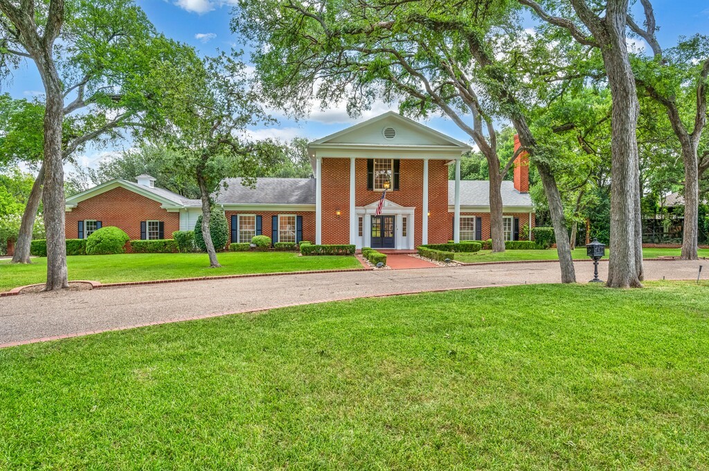 Red-brick building with a columned entrance, mature trees, and a broad lawn.