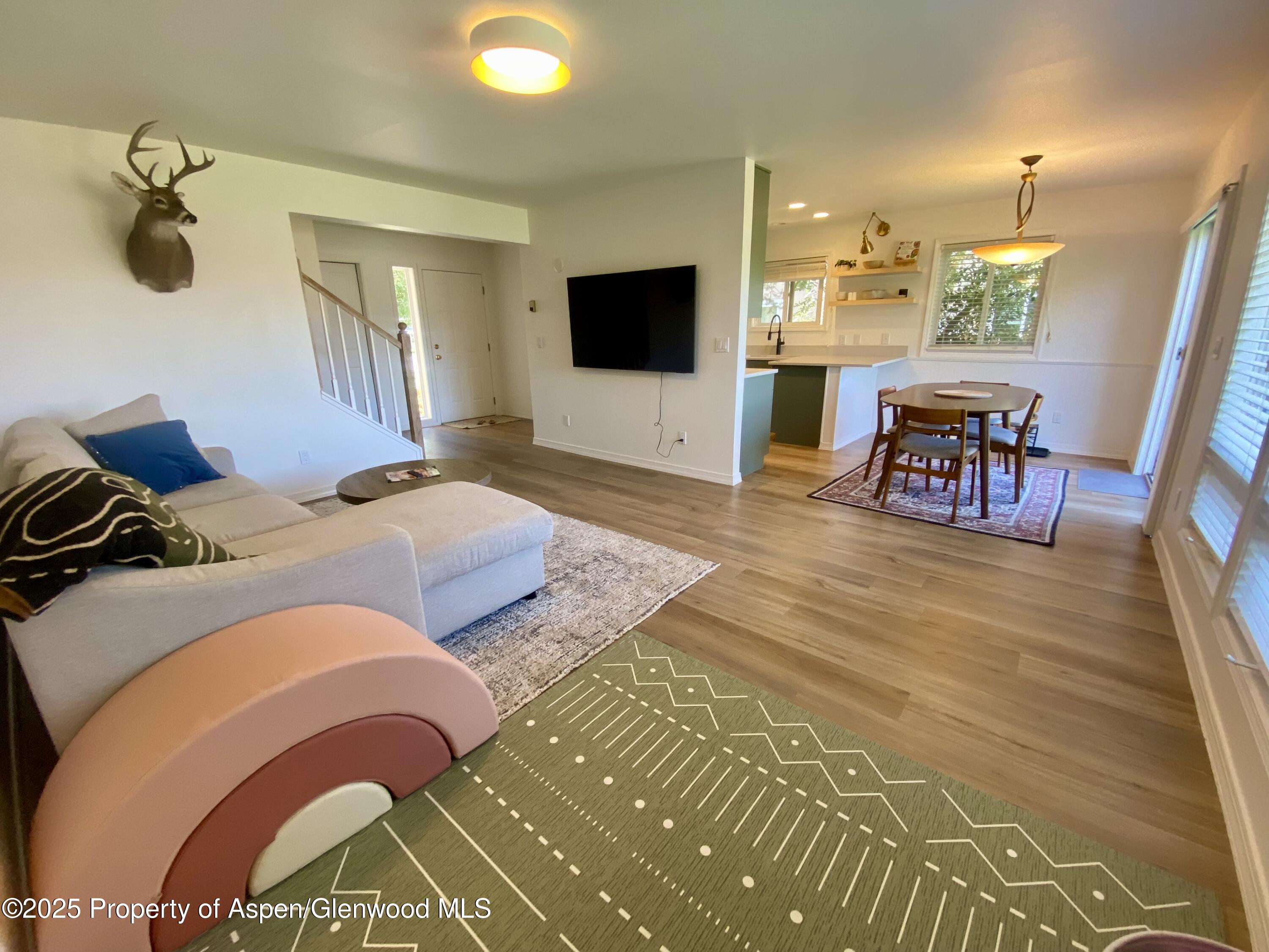 Open-plan living room with a light sectional, mounted television, and adjoining dining area and kitchen.