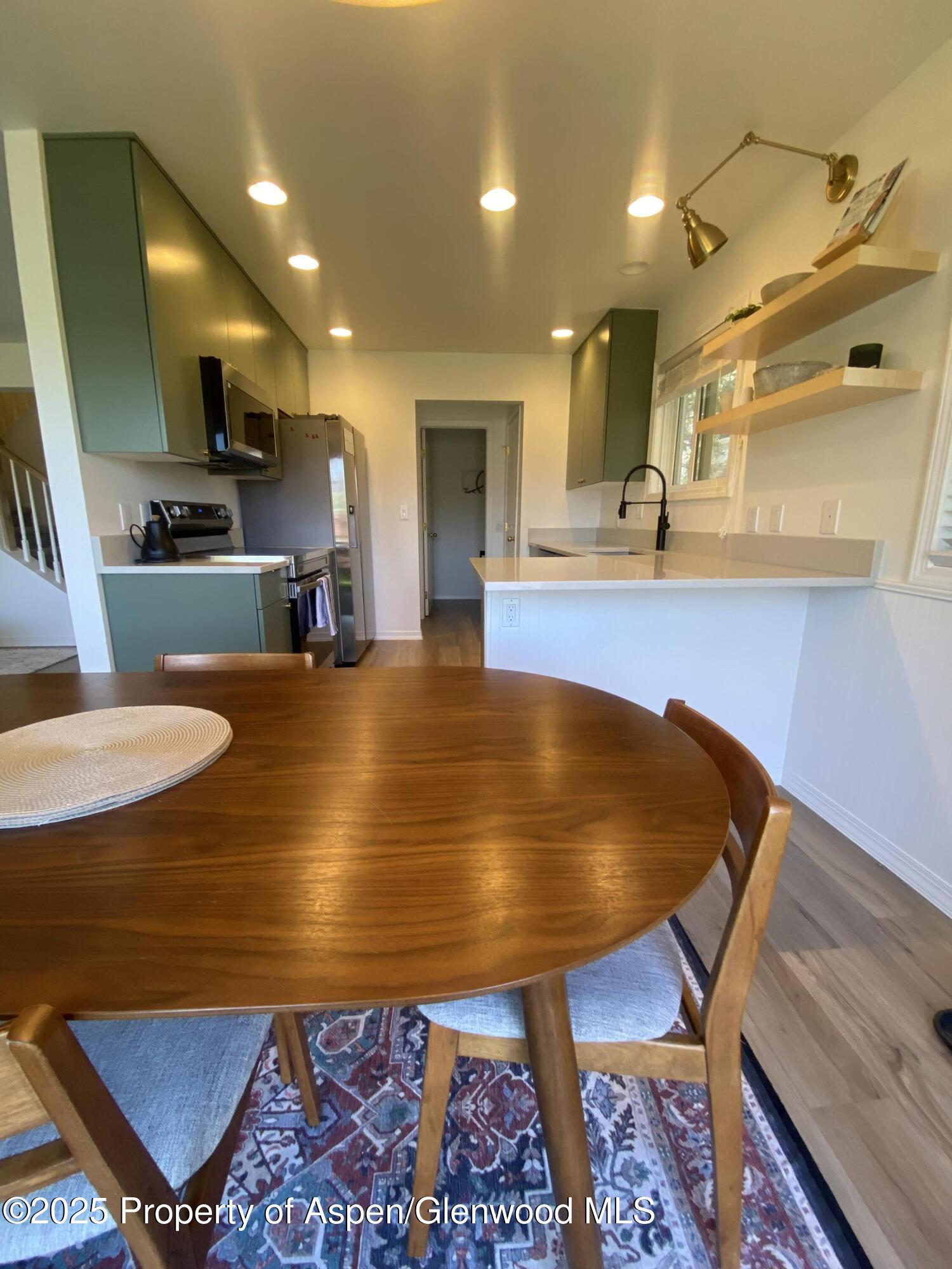 Kitchen with green cabinets, stainless steel appliances, white peninsula, and a round wooden dining table.