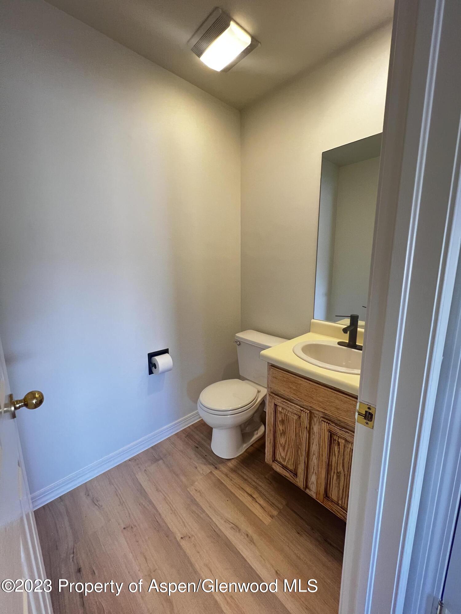 Half bathroom with a wood vanity, oval sink, black faucet, and white toilet.