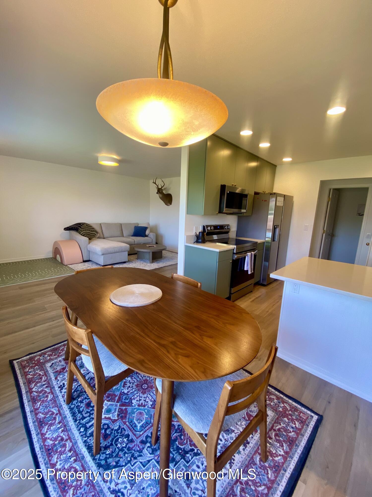 Open-plan kitchen and dining area with green cabinets, a wood table, and living room beyond.