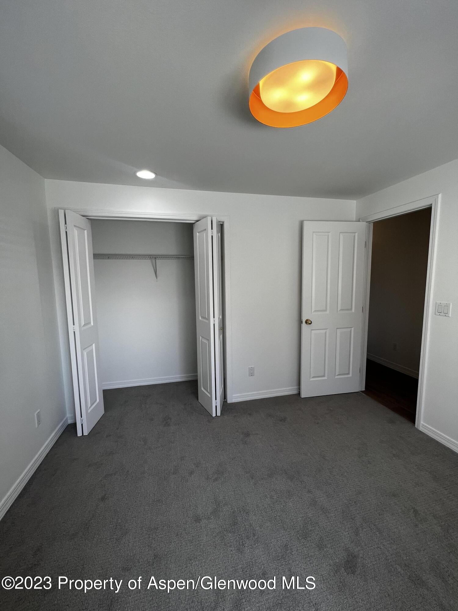 Unfurnished carpeted room with an open closet, doorway, and bright orange ceiling light.