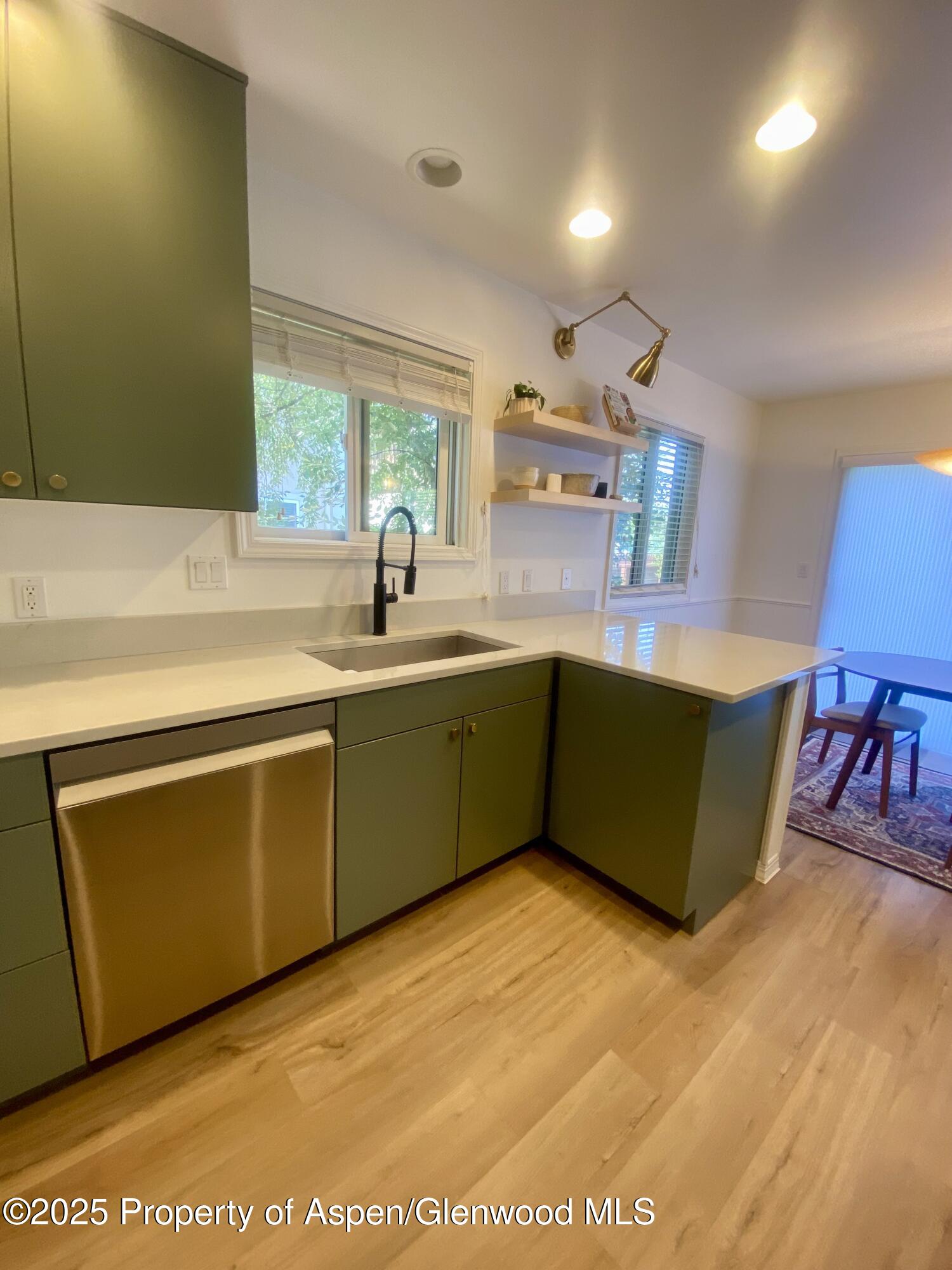 Kitchen with green cabinets, white counters, and a peninsula beside the dining area.