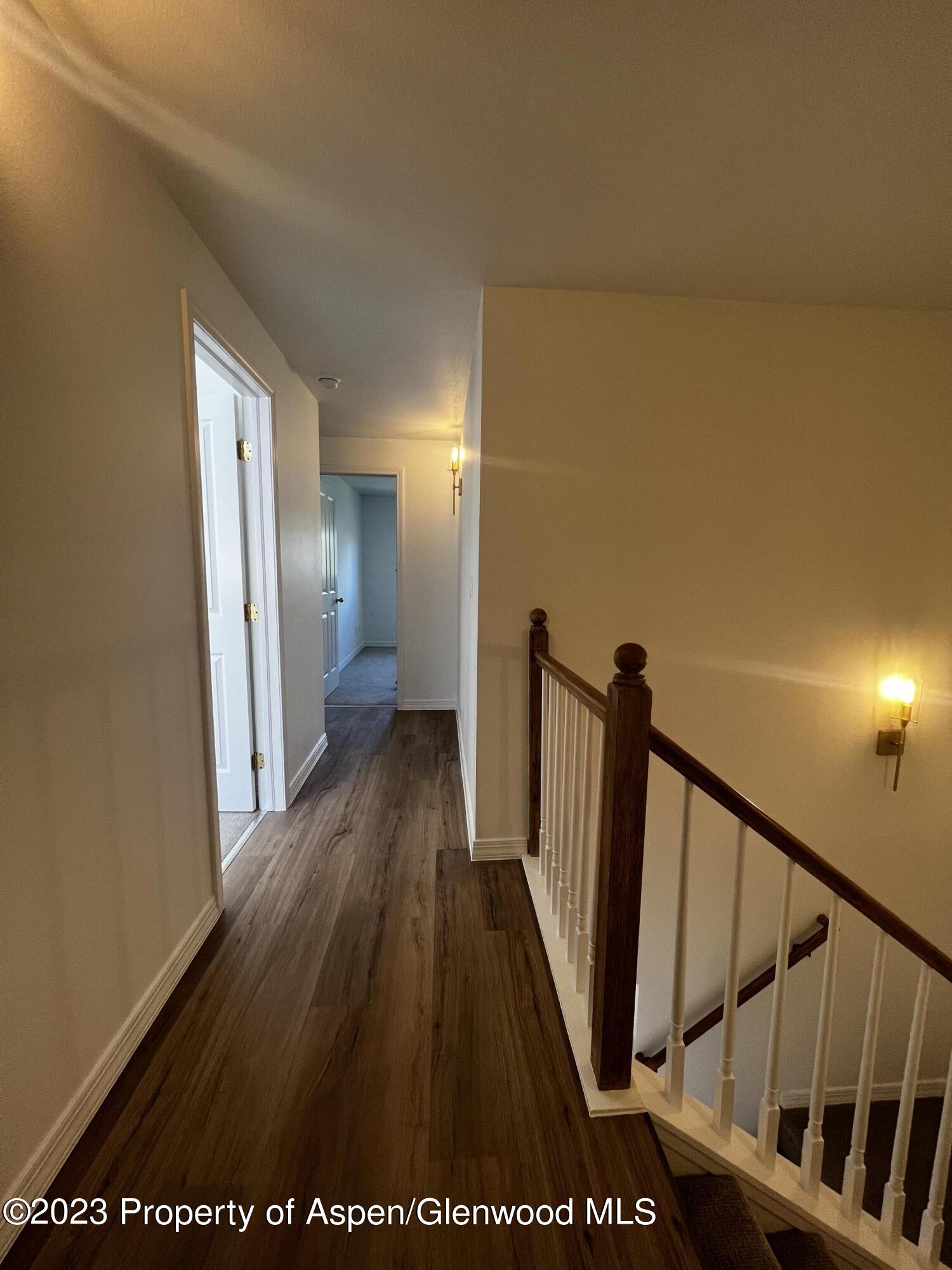 Upstairs hallway with wood-look flooring and a staircase with white balusters and dark wood railing.