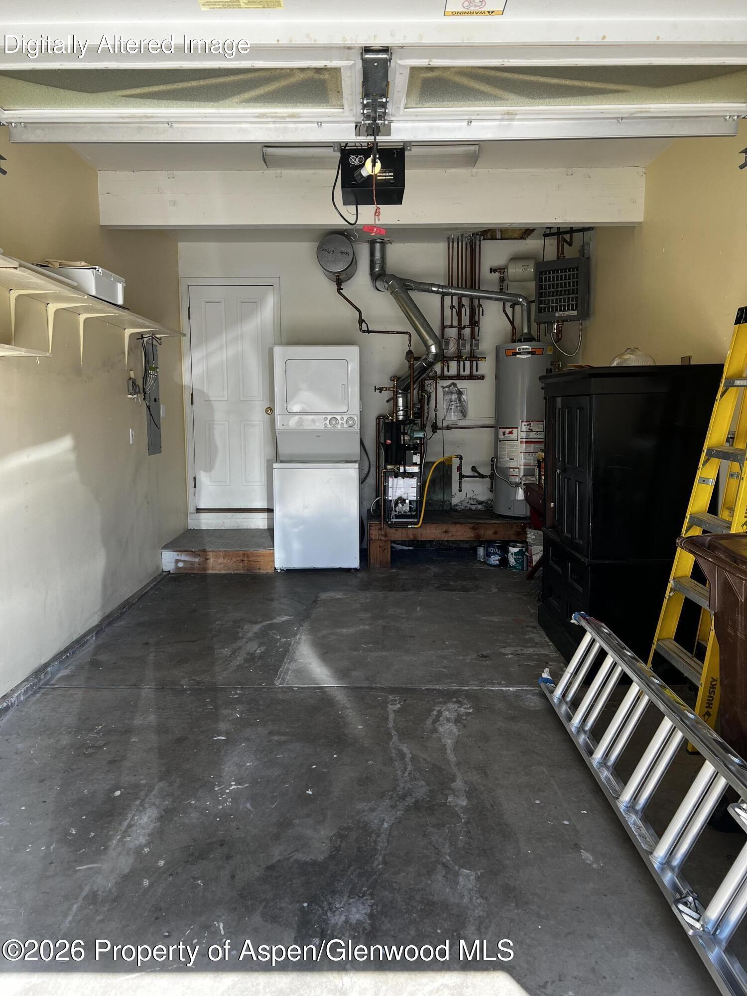 Garage with concrete flooring, laundry appliances, exposed mechanical equipment, storage cabinets, and ladders.